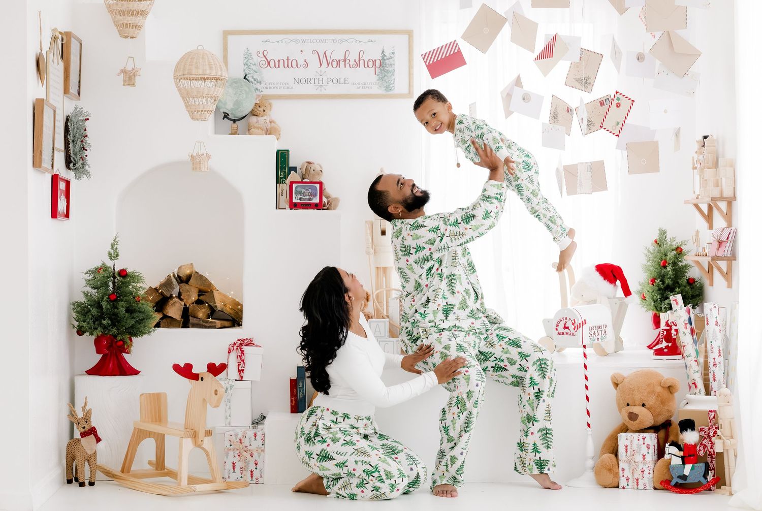 Family in matching green Christmas pajamas posing in festive white studio with holiday decorations and Santa's Workshop sign.