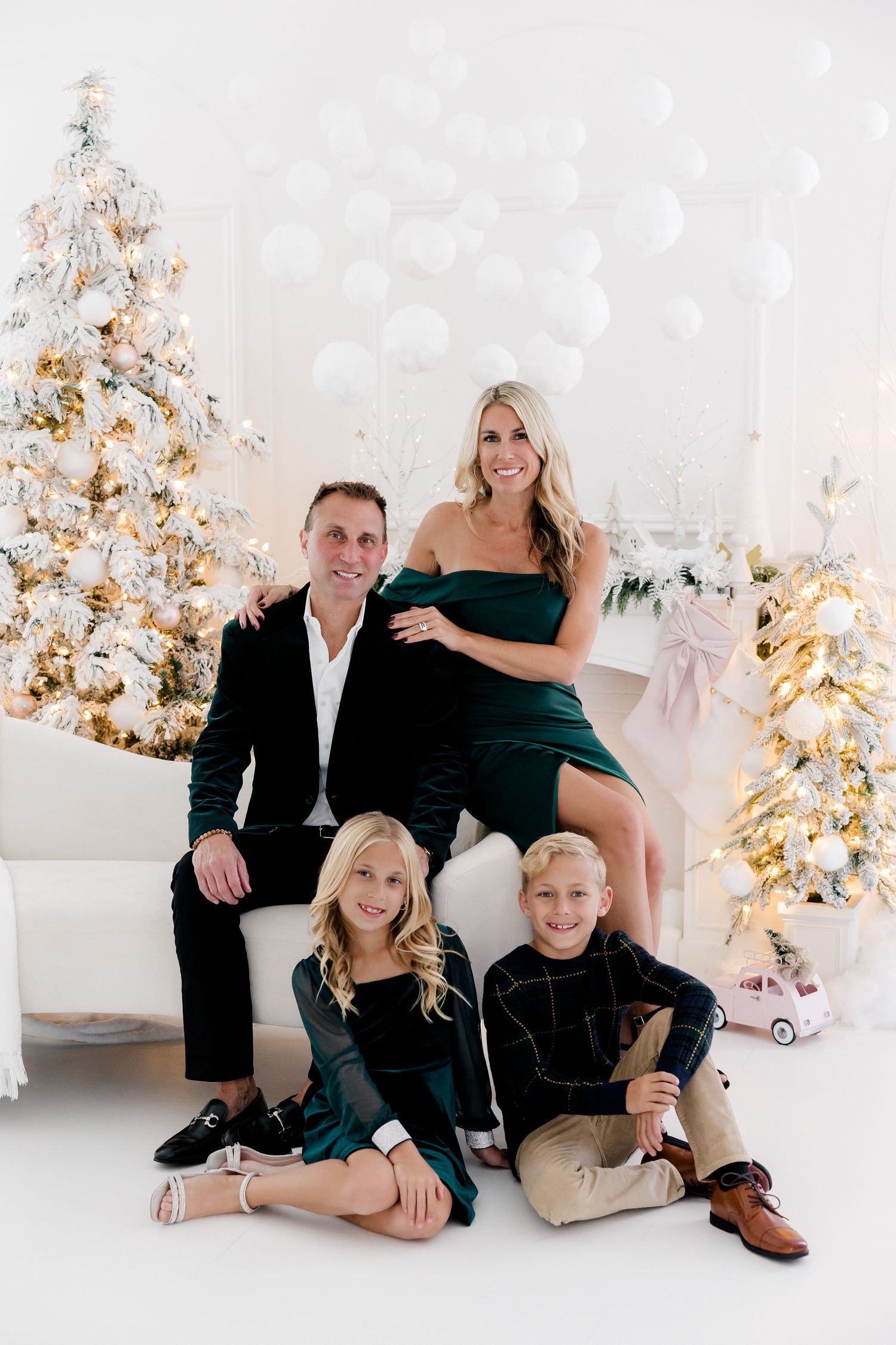 Family holiday portrait session in coordinated black and neutral outfits against white Christmas backdrop.