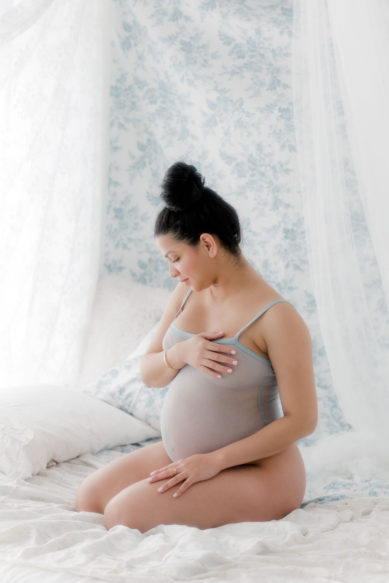 Intimate maternity portrait in gray against soft floral backdrop.