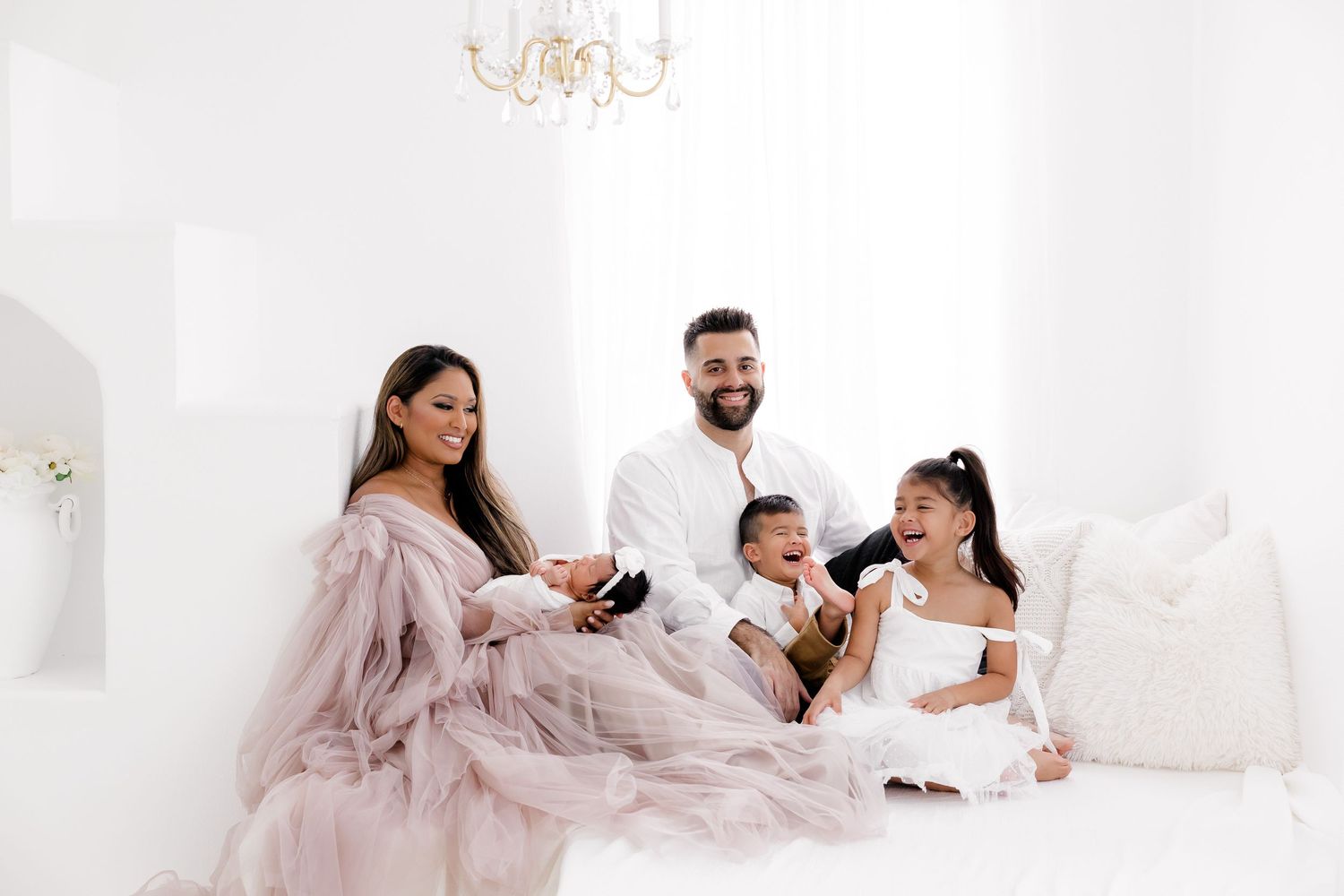 Elegant family photoshoot with mother in pink dress and white decor.