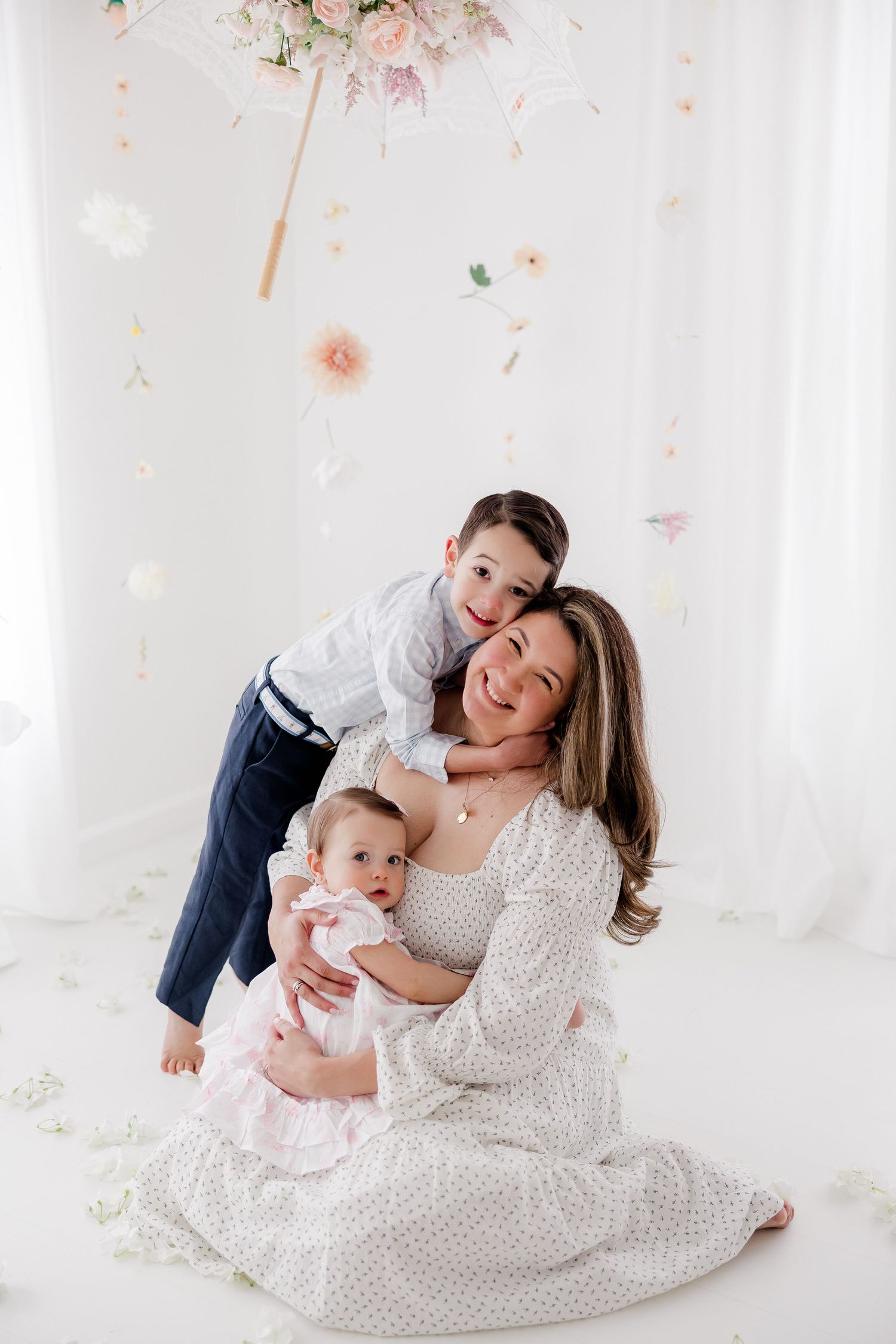 A family in matching white outfits shares tender moments during a photo session with delicate pink floral decorations.