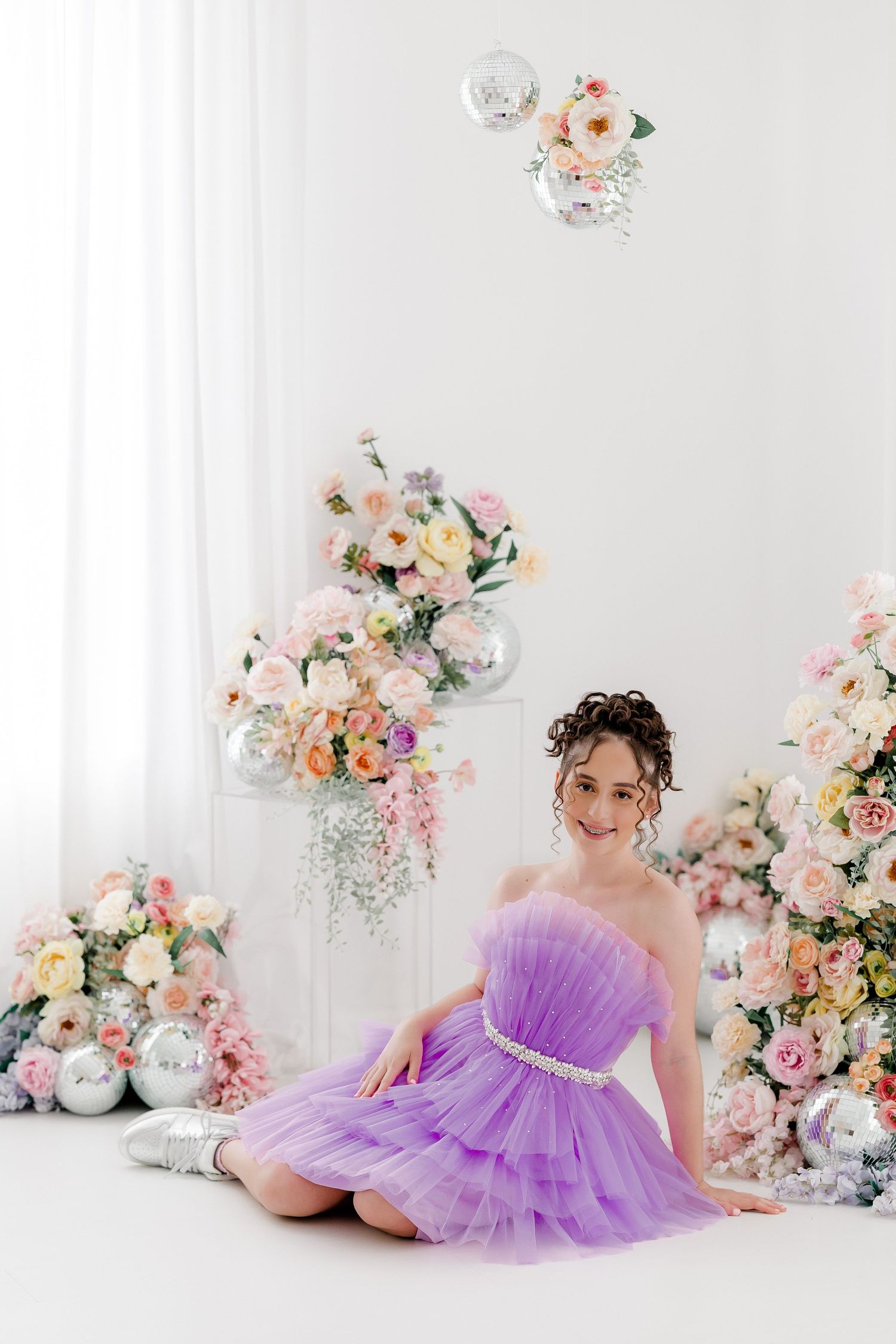 Elegant purple tulle dress photographed in white studio setting with romantic floral arrangements and balloon decor.