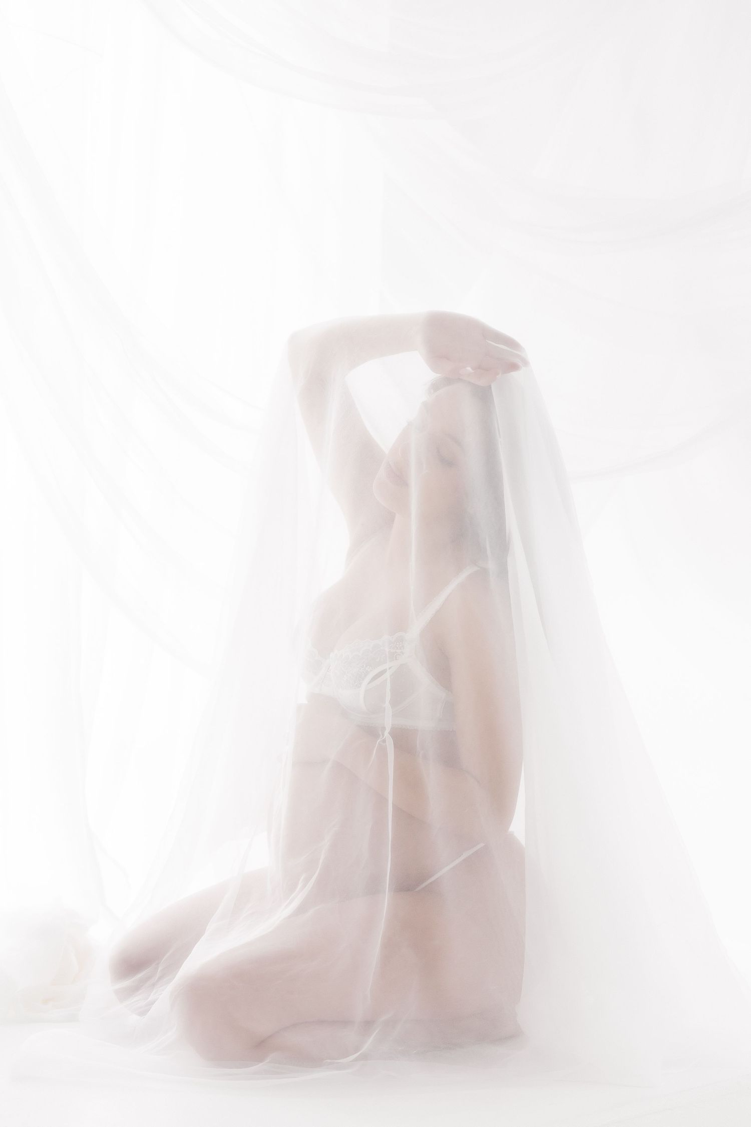 Artistic silhouette of a figure draped in sheer white fabric creating an ethereal, dreamy effect against a light background.