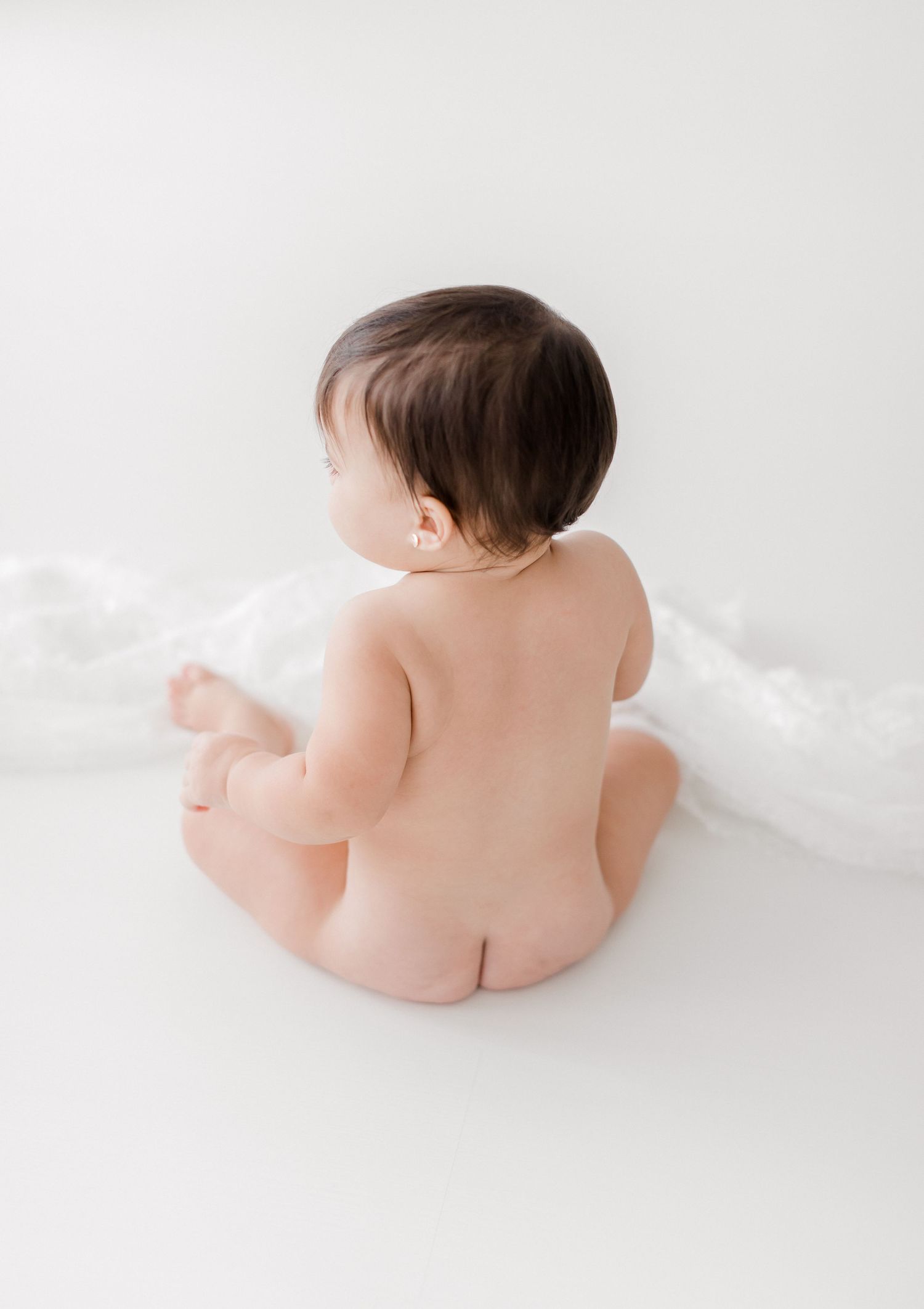 Baby in white setting photographed from multiple angles showing developmental milestones of rolling over.