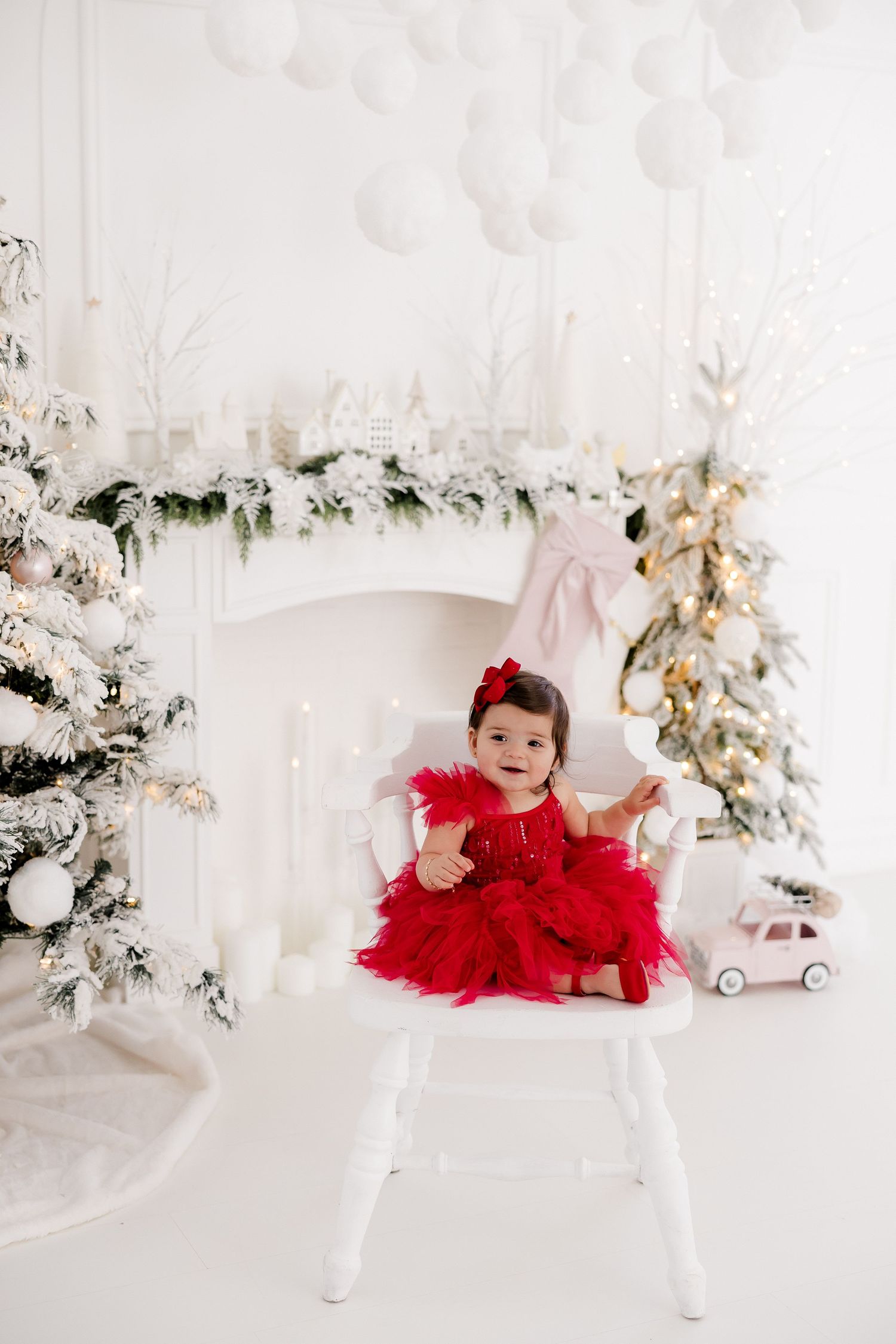 Child in red tulle dress playing on white bench with Christmas decorations in background.