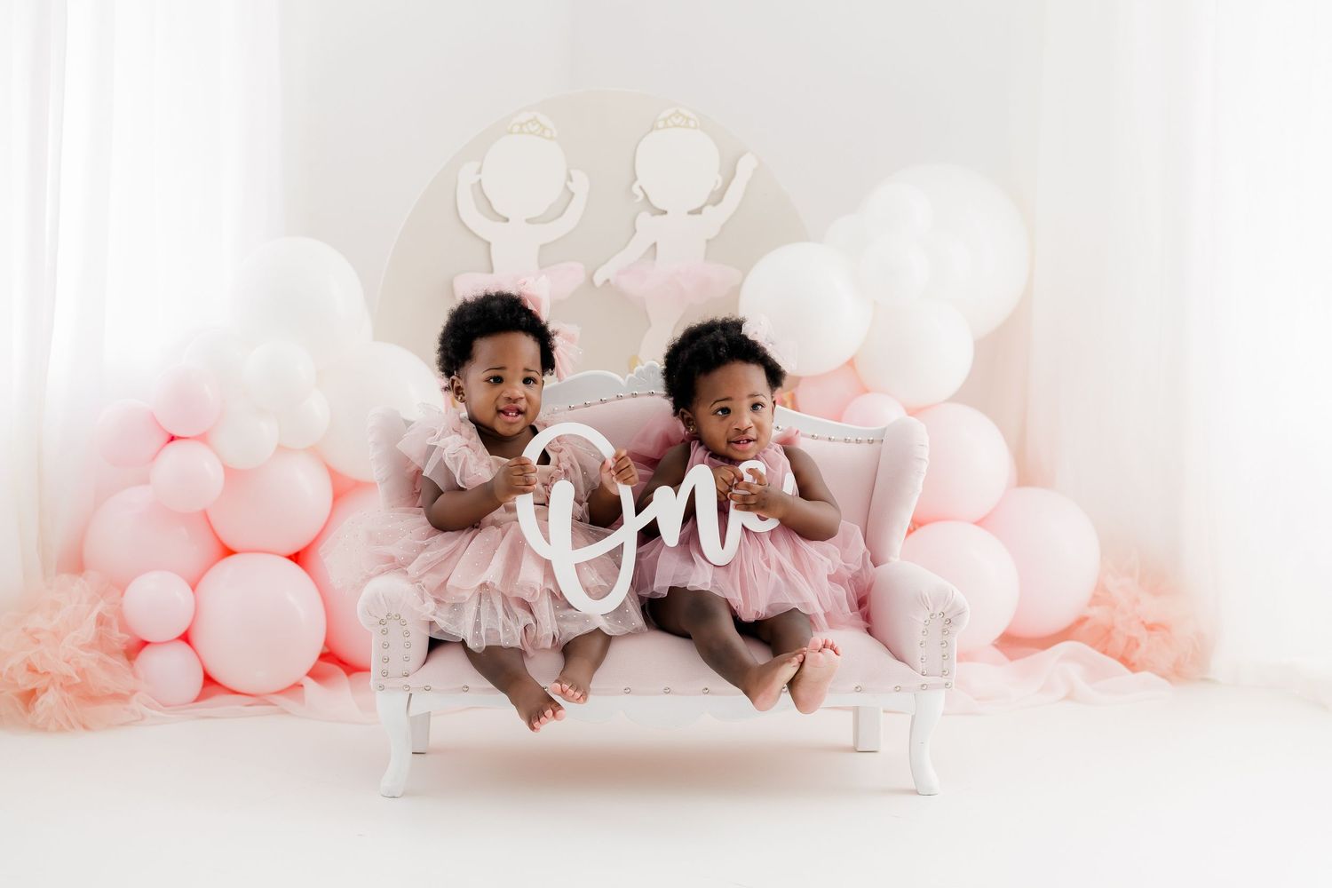 Studio portrait session with pink balloon decorations against white backdrop.