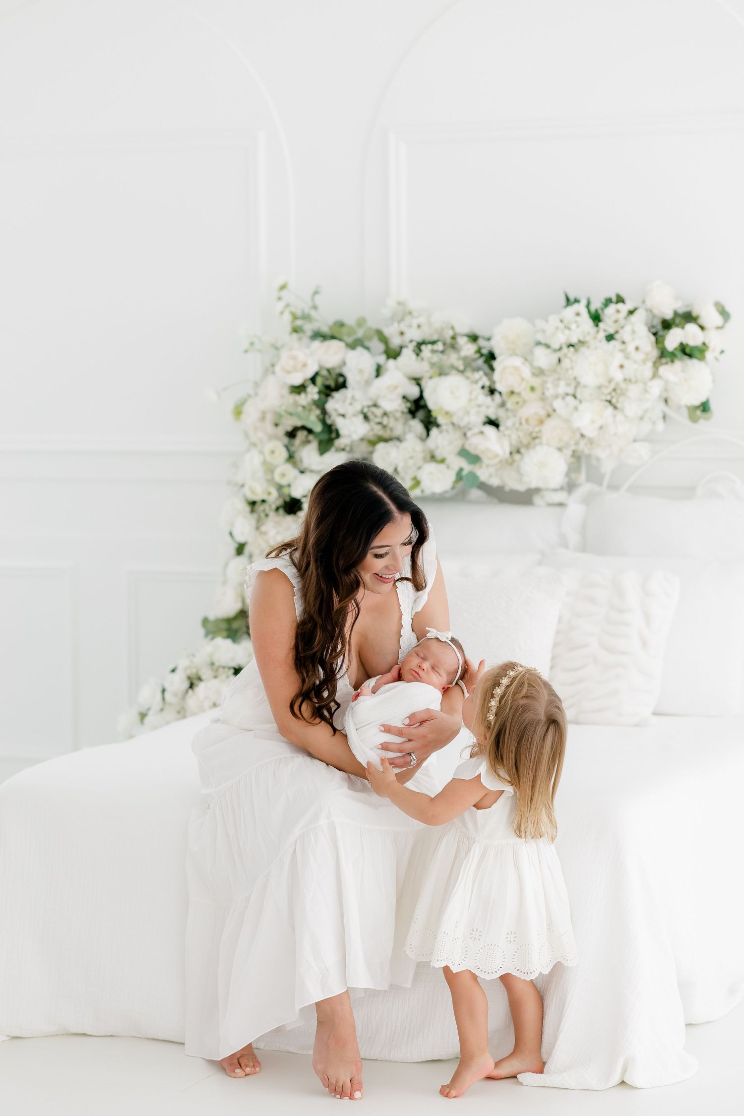 Family portrait session in all white with floral backdrop showing tender moments together.