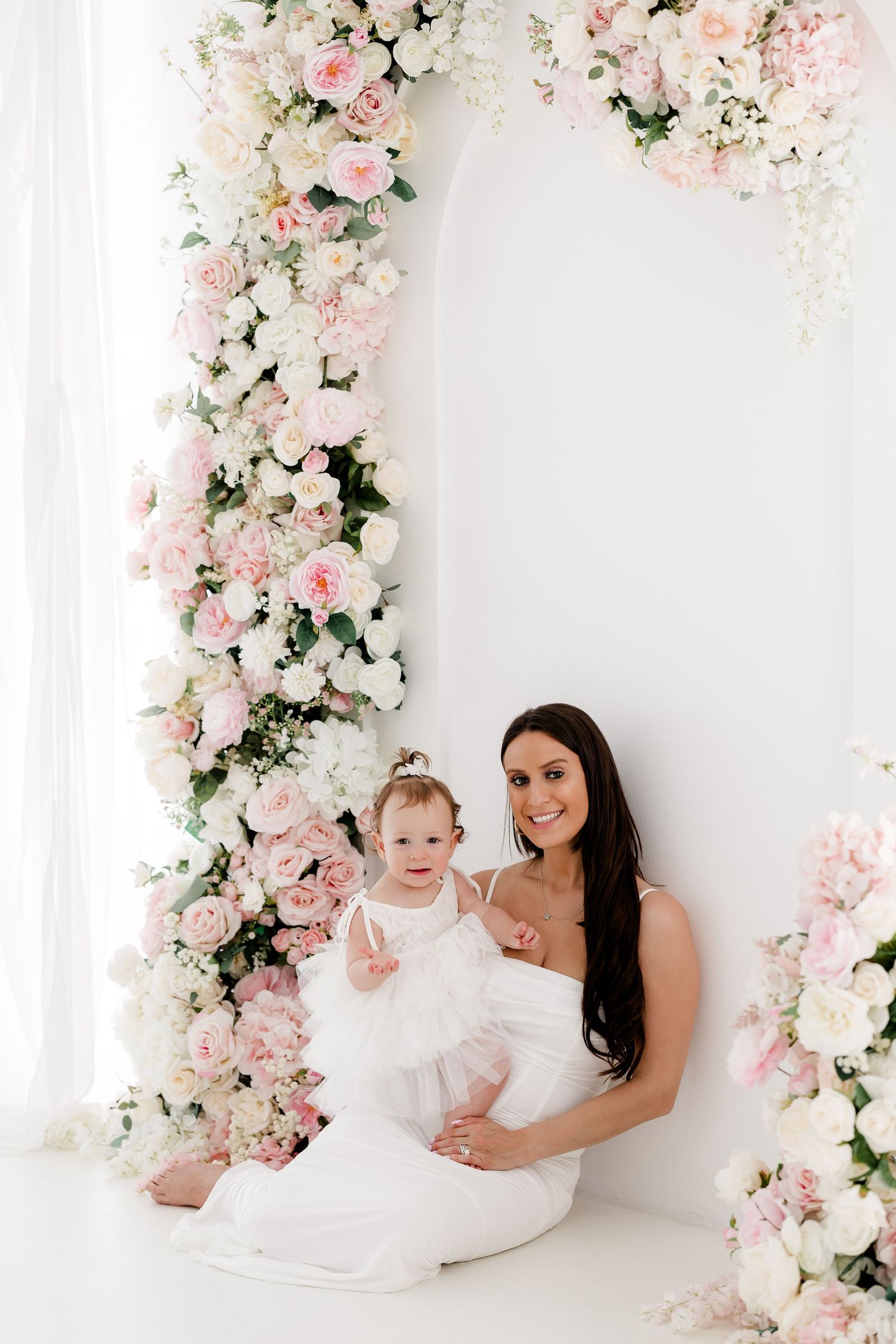 Beautiful floral arch with pink and white roses frames a tender moment against a white backdrop.