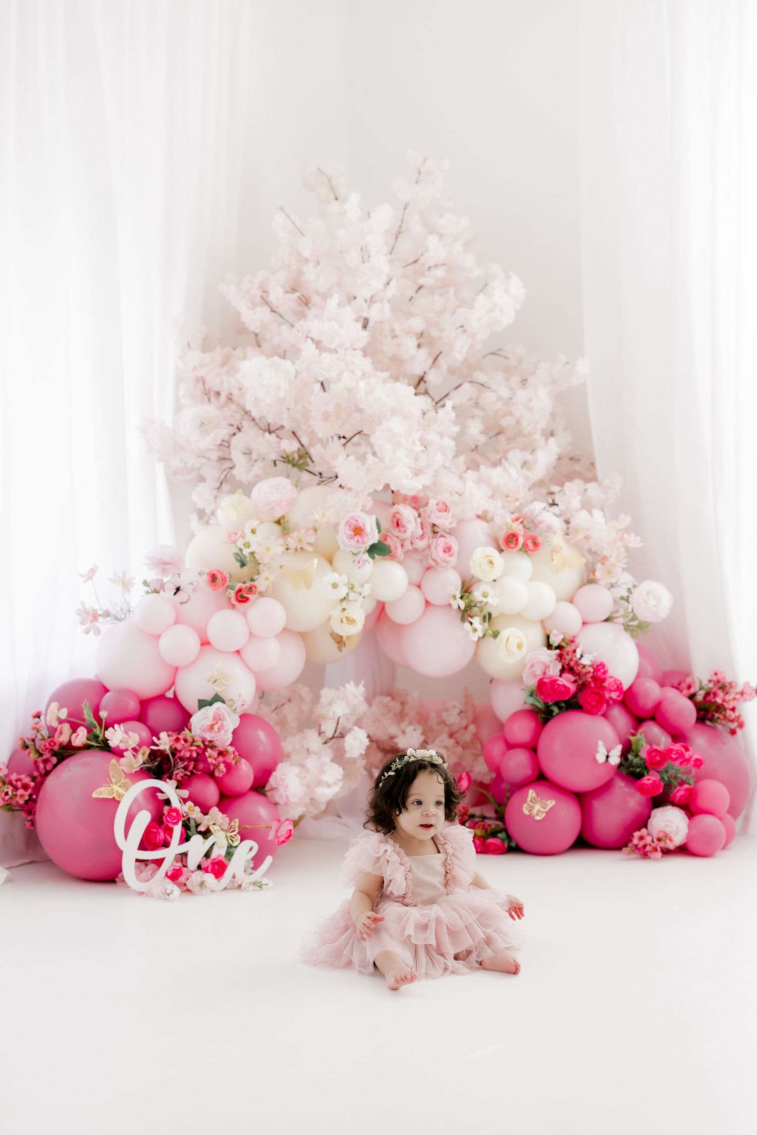Pink and white floral arrangements with balloons create a soft, romantic backdrop for photography sessions.