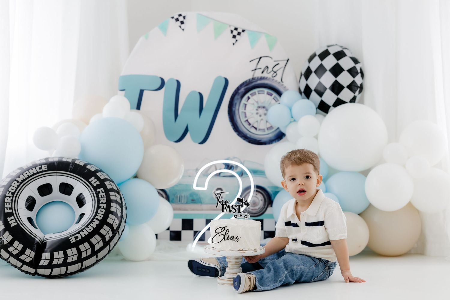 Racing themed first birthday photo session with blue balloons and checkered flag decorations.