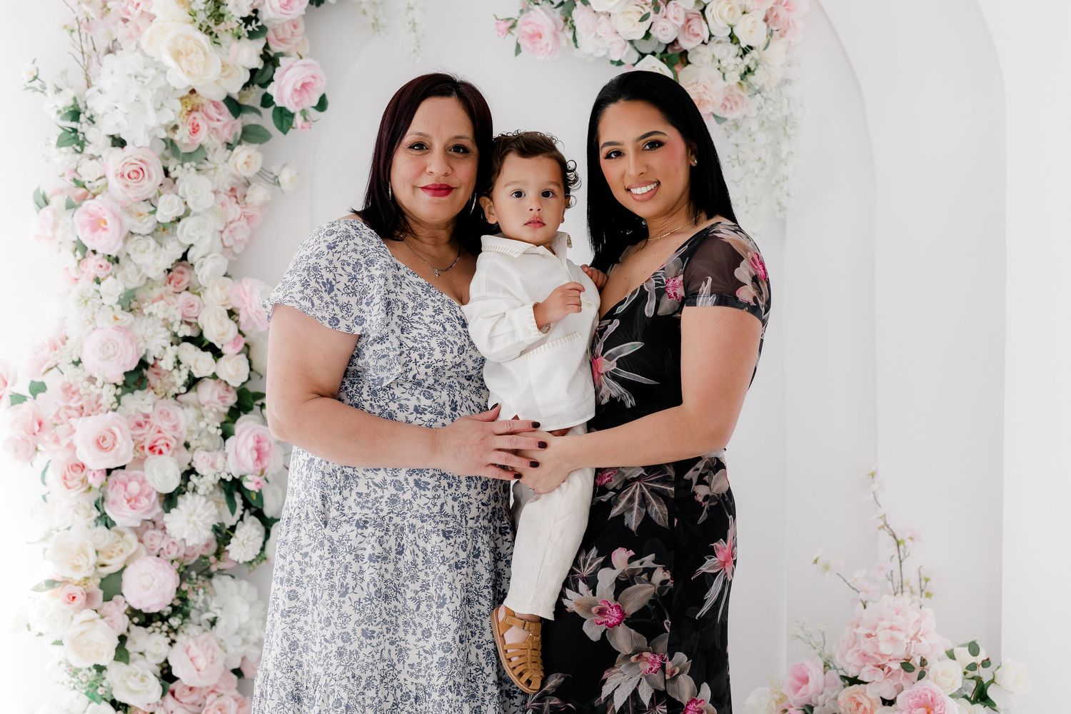 Three generations pose together against a floral backdrop with pink and white cherry blossoms.