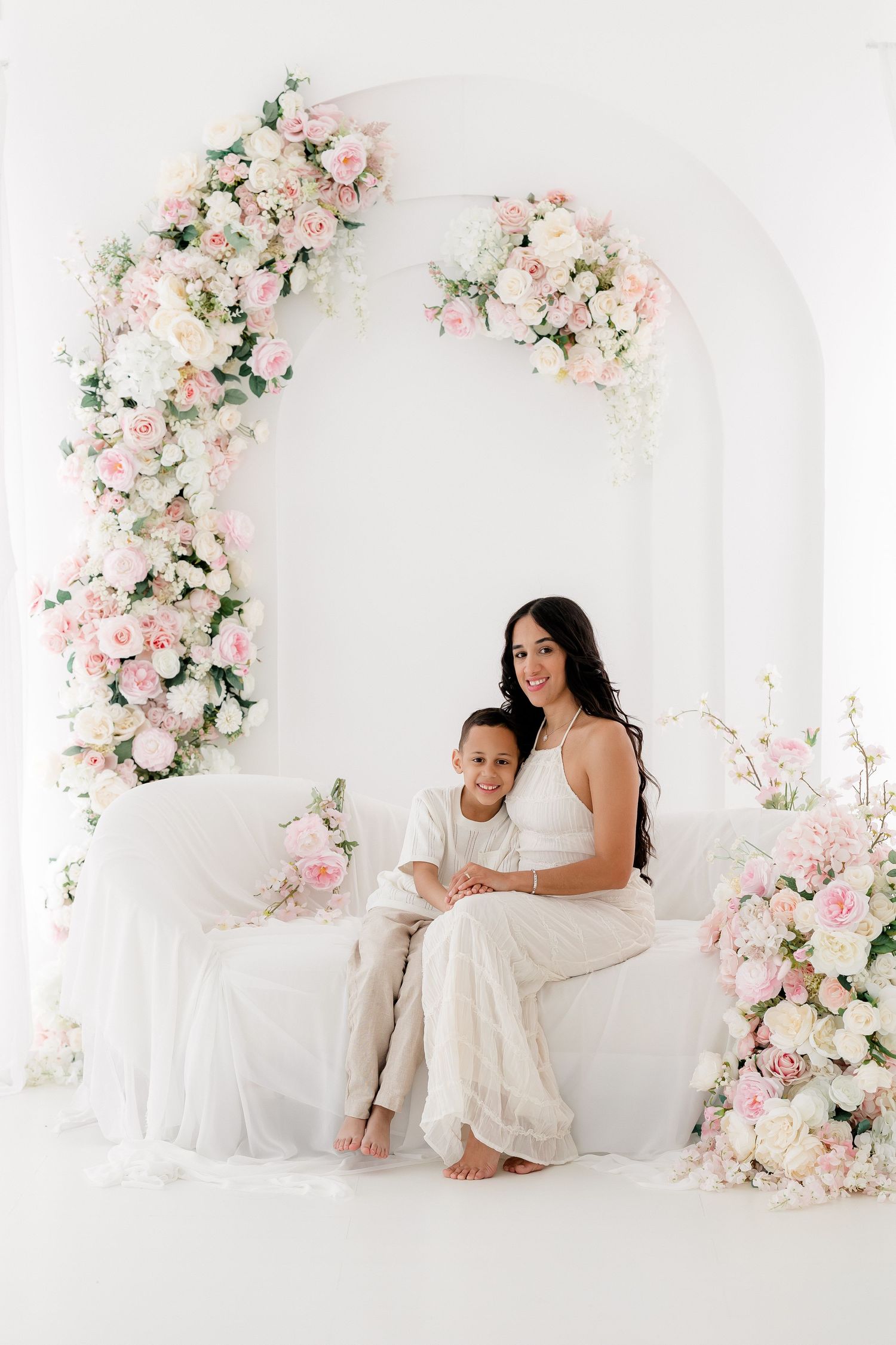 Elegant white studio setting with romantic pink and white floral arrangements framing a cozy seating area.