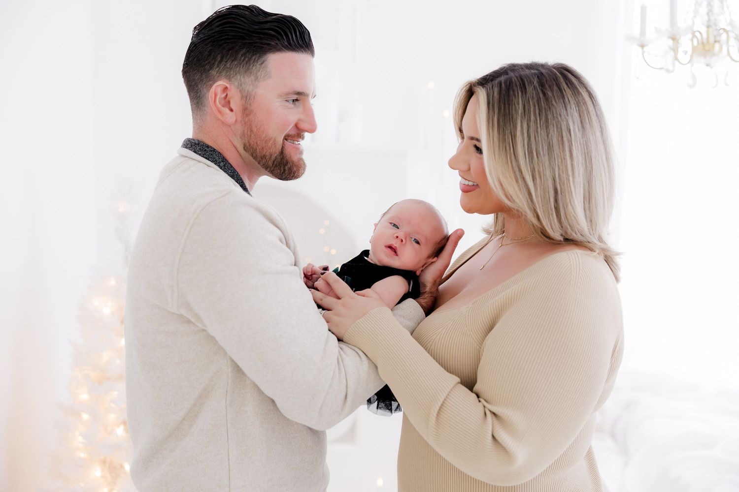 Family sharing tender holiday moments in cream outfits against white backdrop with Christmas decor.