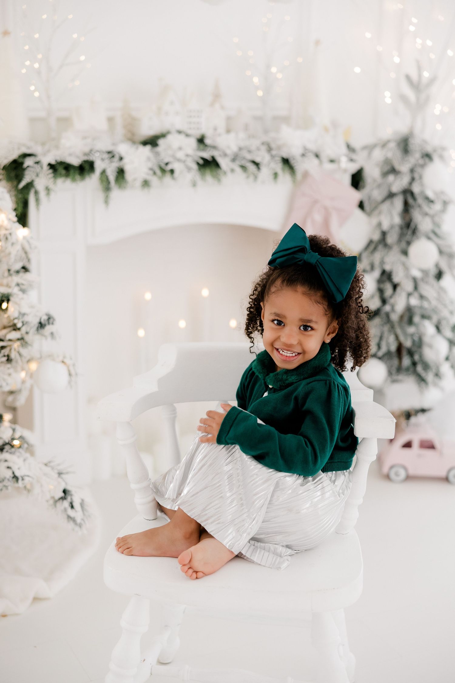 Child in emerald green outfit lying playfully on white floor in elegant winter studio setting.