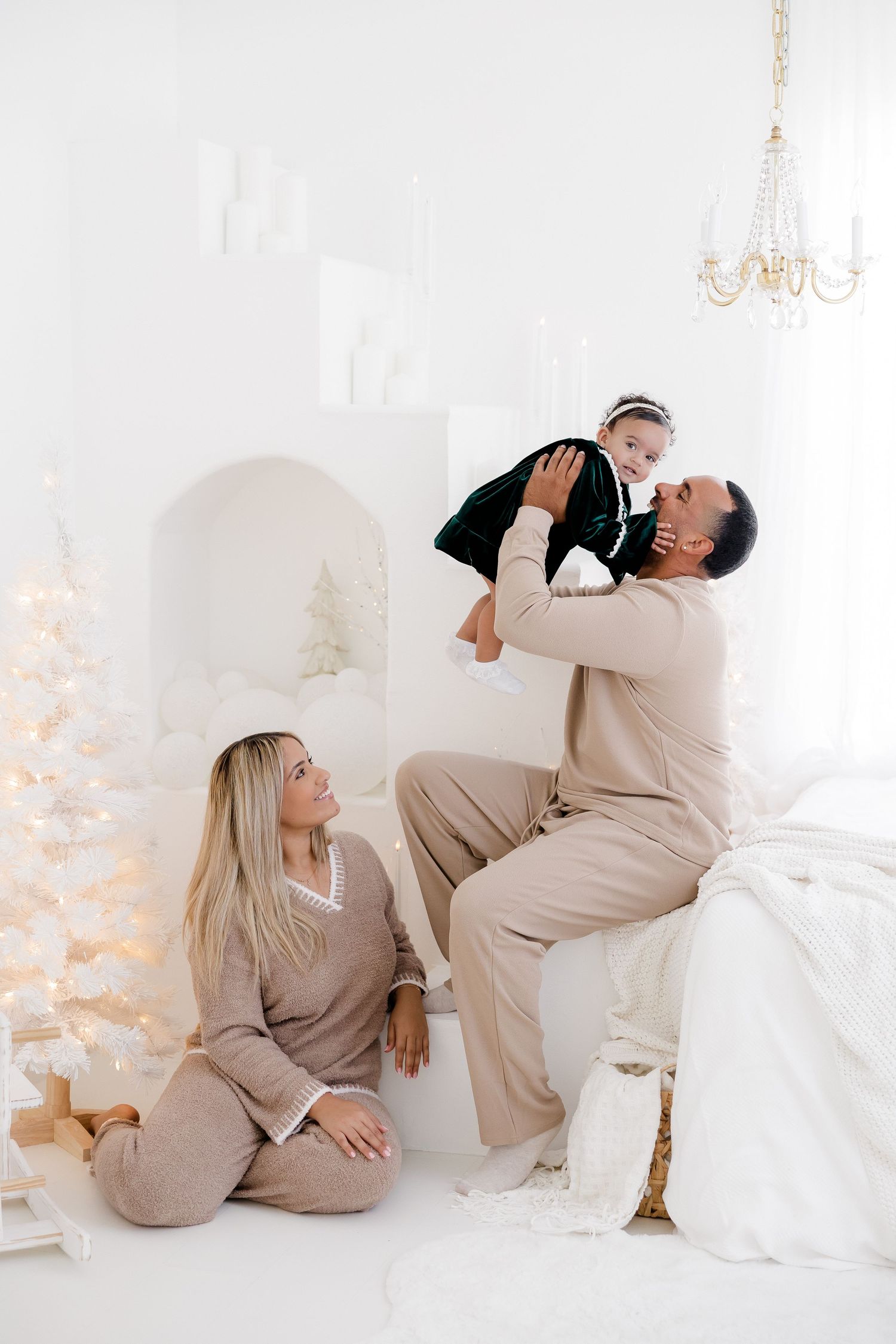 Family in neutral beige outfits posing playfully in white Christmas studio setting.