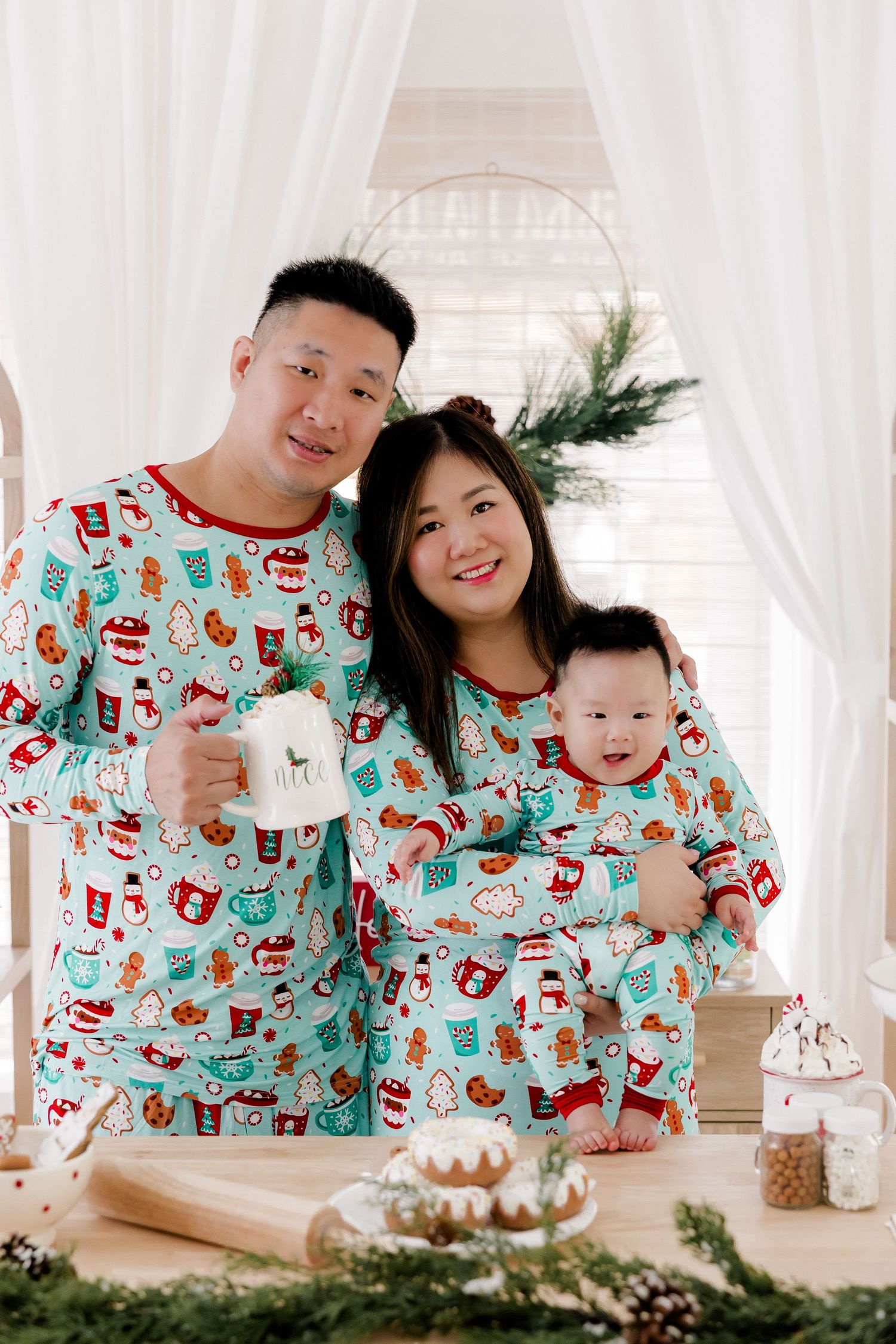 A family wearing matching holiday pajamas poses together in a bright white studio setting.