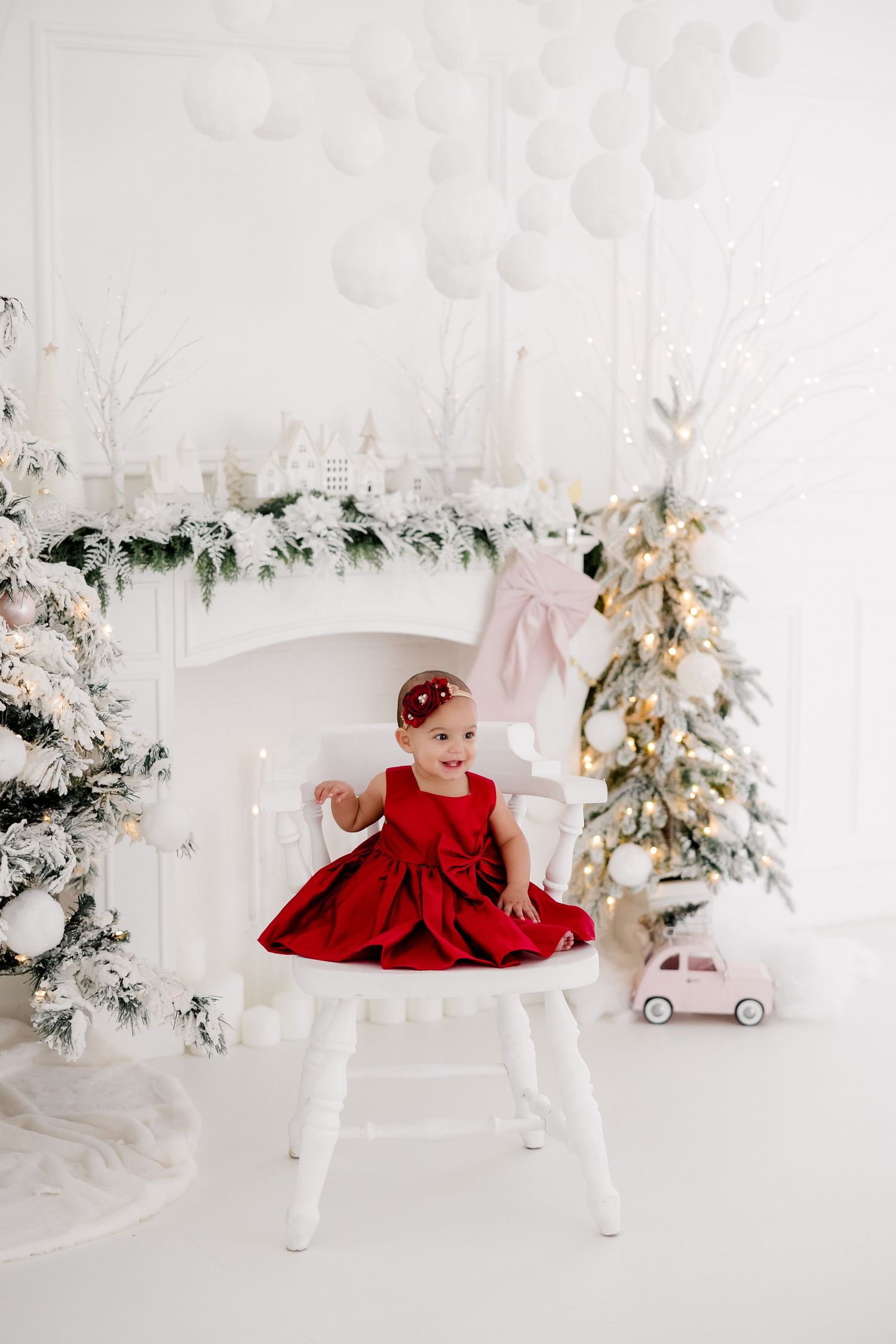 Festive holiday scene with red dress against white decor, Christmas trees, and toy car.