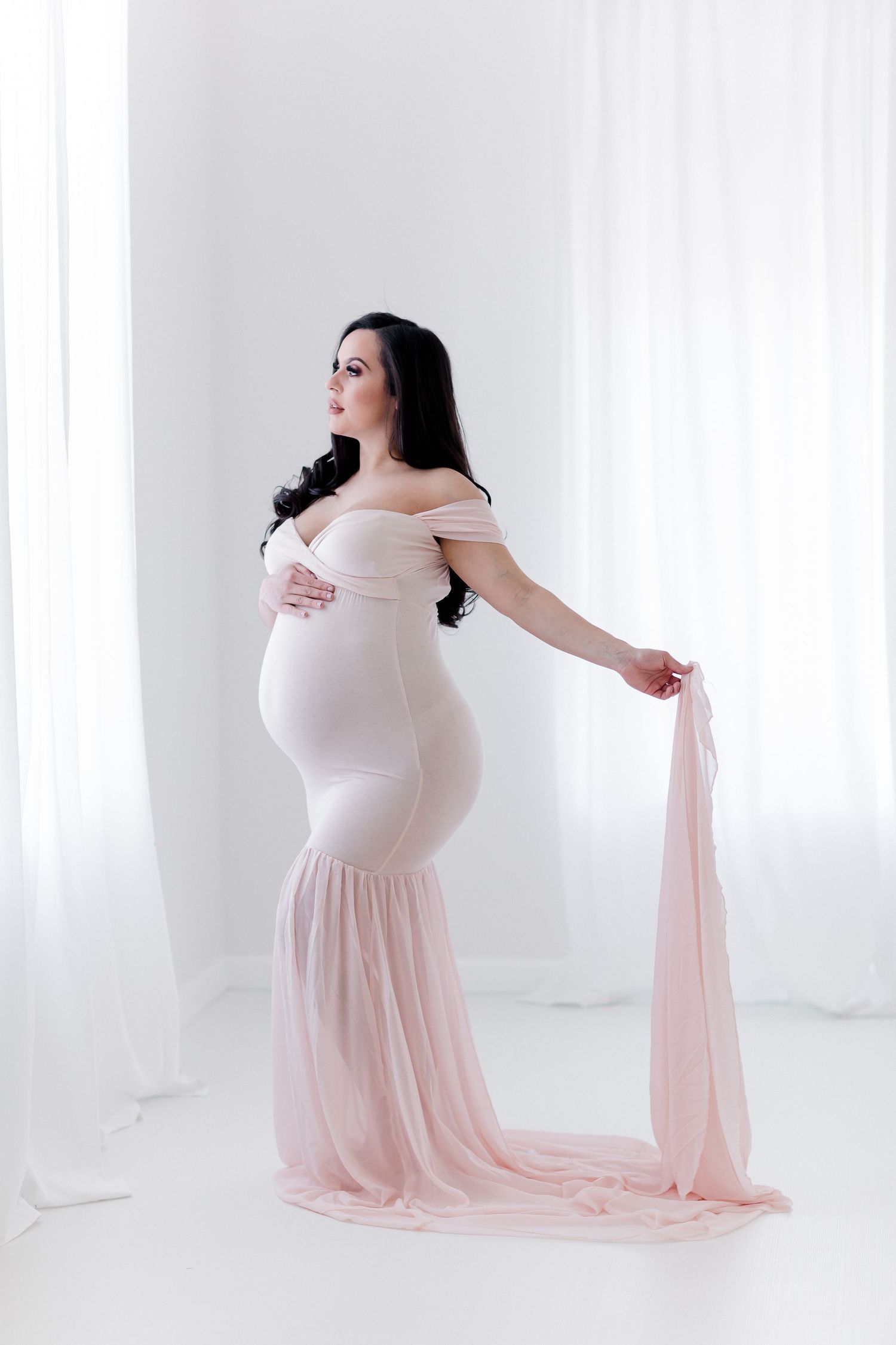 Flowing pink and white maternity gown captured in bright studio setting.