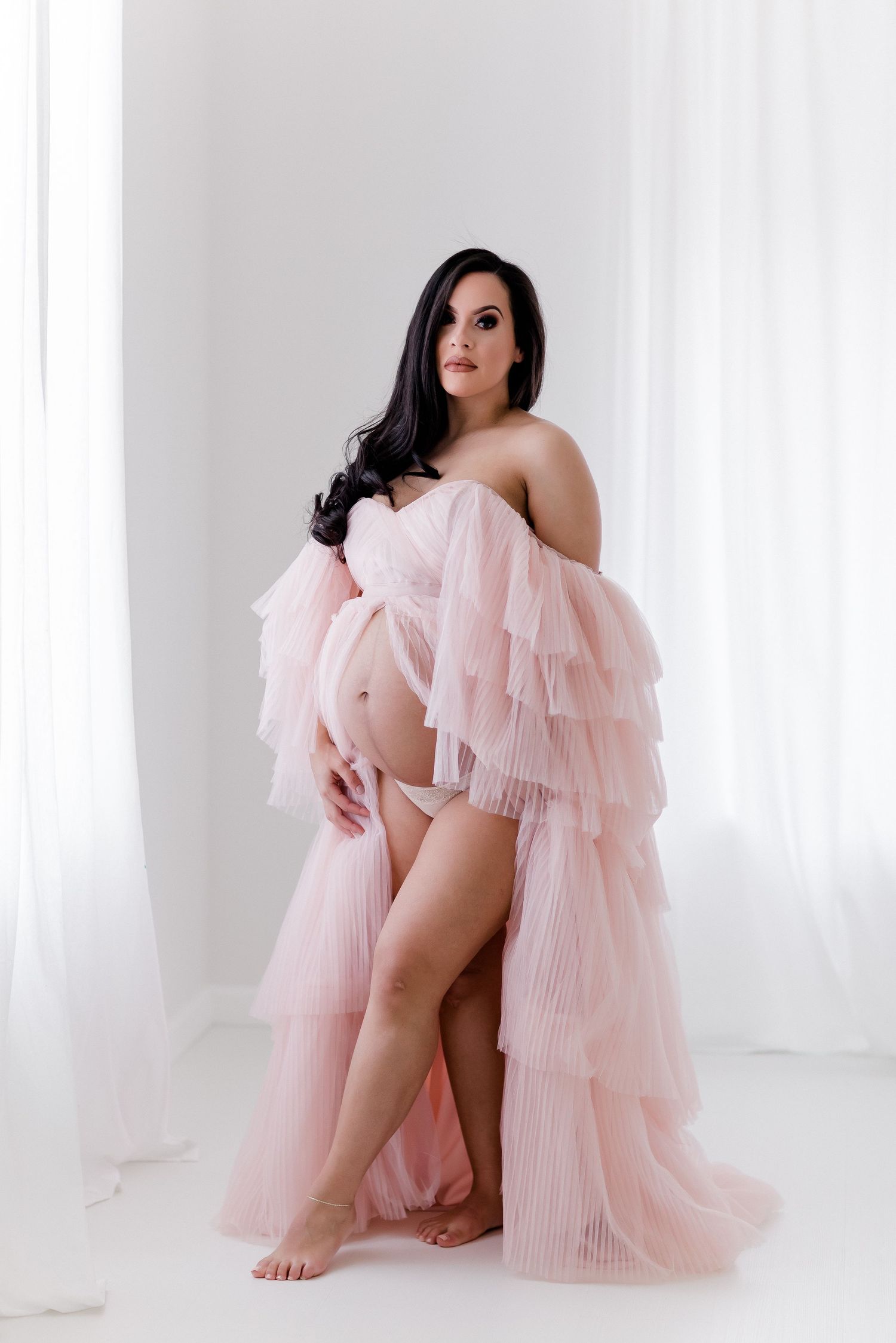 Artistic boudoir photography with pink pleated tulle robe in bright studio setting.