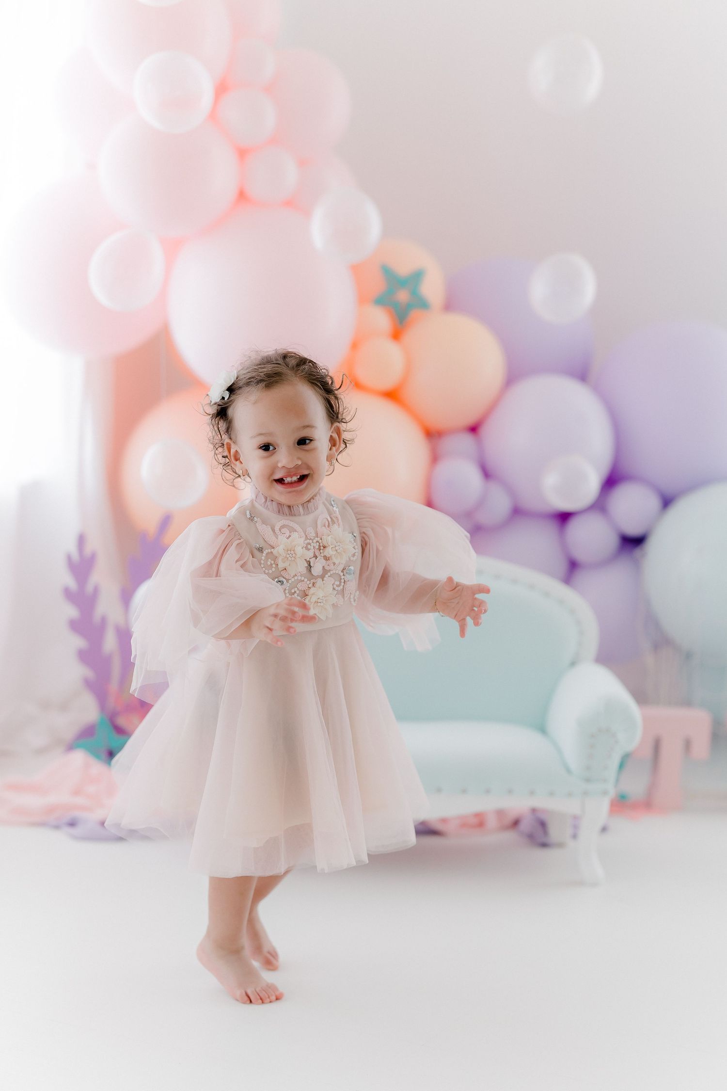 Whimsical studio setup with pastel balloons and vintage furniture against soft backdrop.