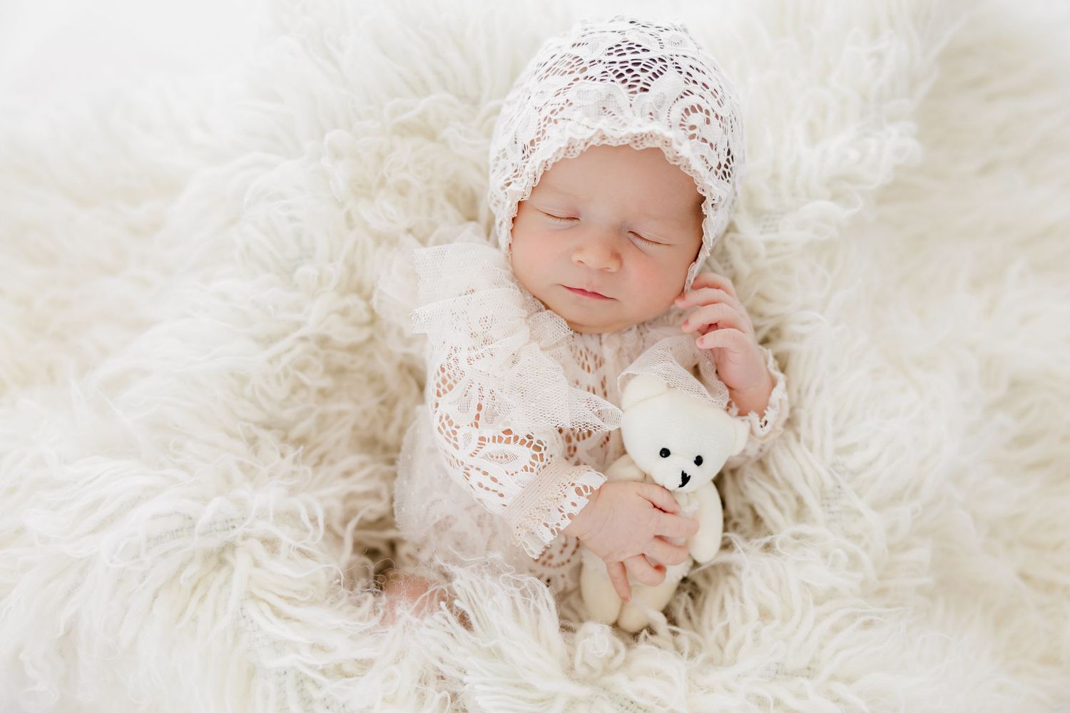 Sleeping newborn in delicate lace bonnet photographed on soft white fur.