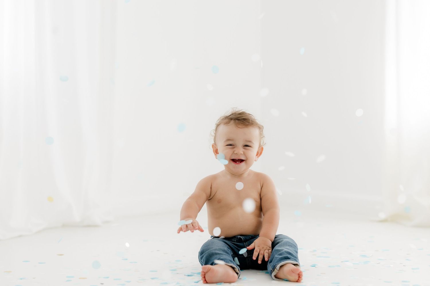 A baby in blue jeans sits on a white background, showing a range of playful expressions and poses.