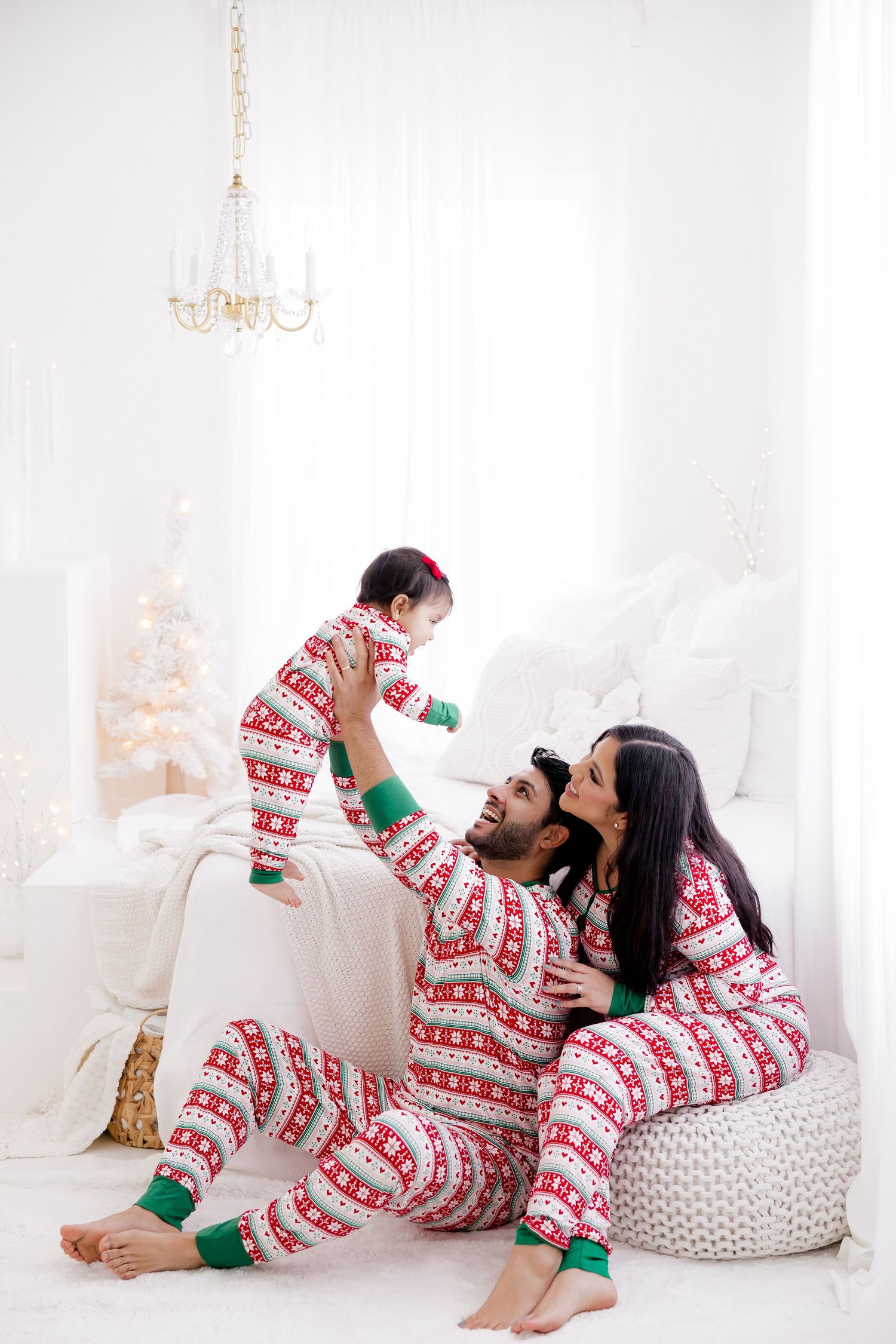 Family in matching holiday pajamas relaxing on white furniture with Christmas decorations.
