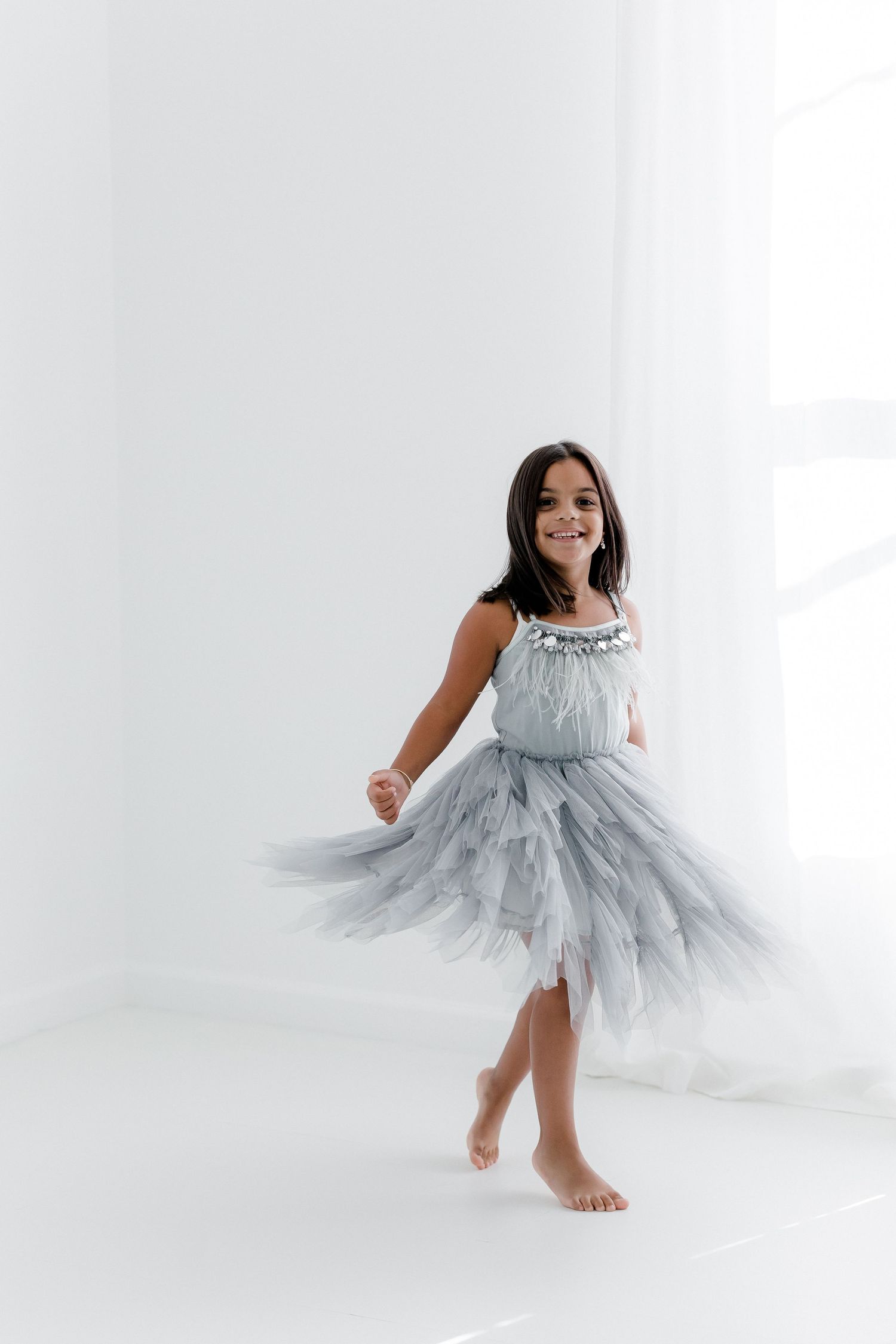 Dancer in flowing grey tulle dress twirls gracefully in bright studio setting.