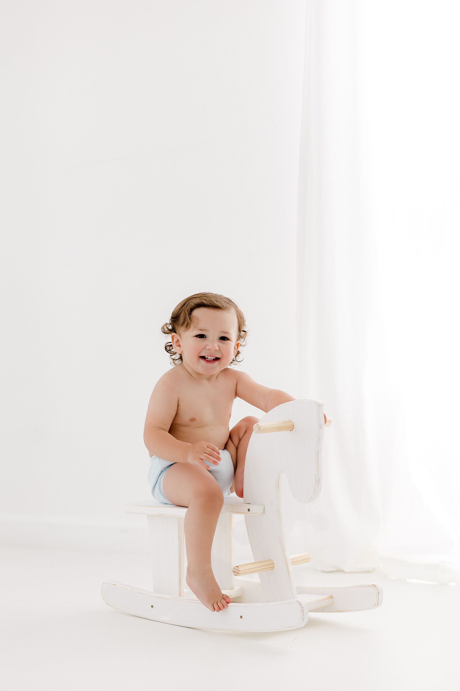 Baby in diaper plays with white furniture during studio photoshoot.