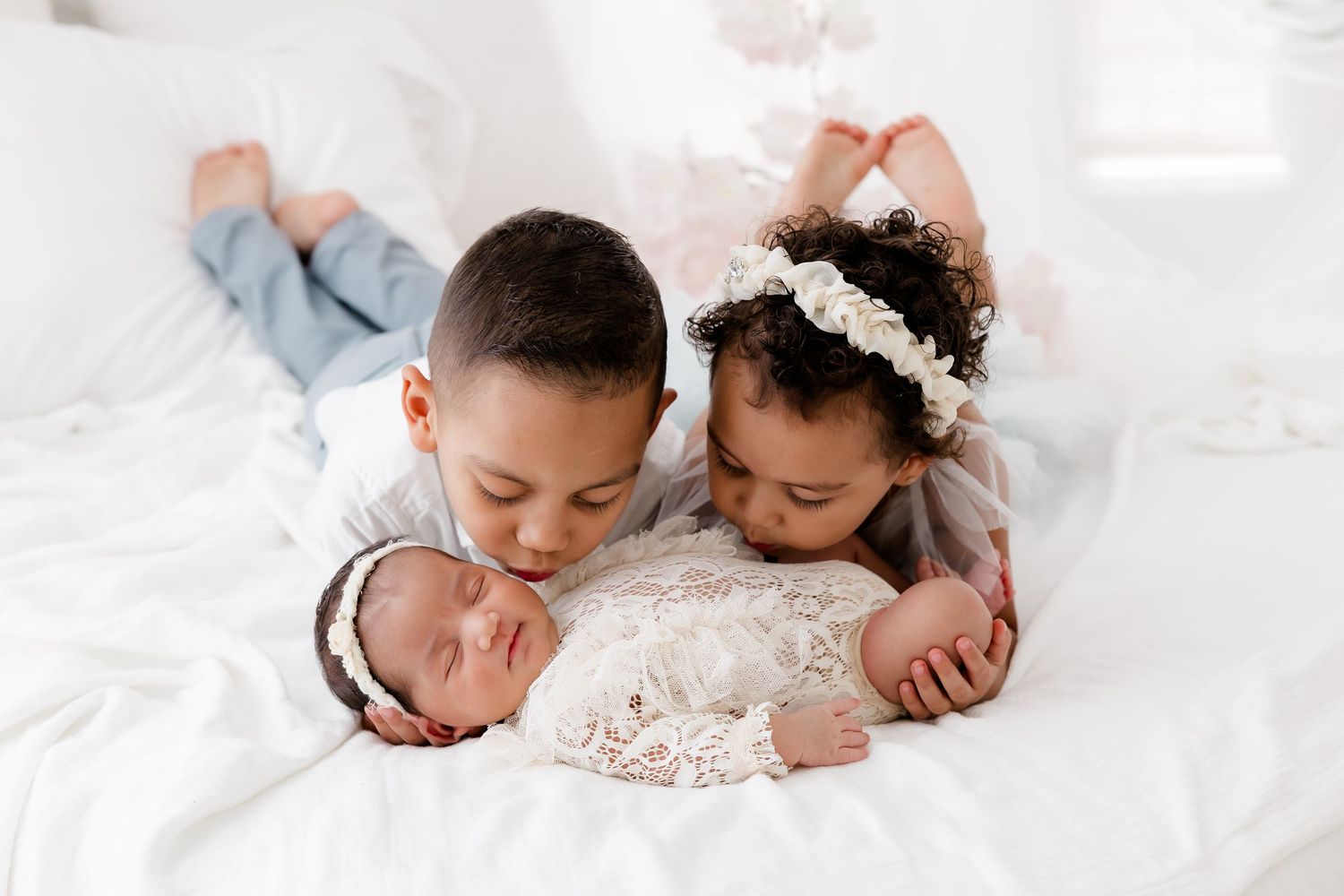 A sleeping baby lies on white bedding wearing a delicate lace dress and floral headband.