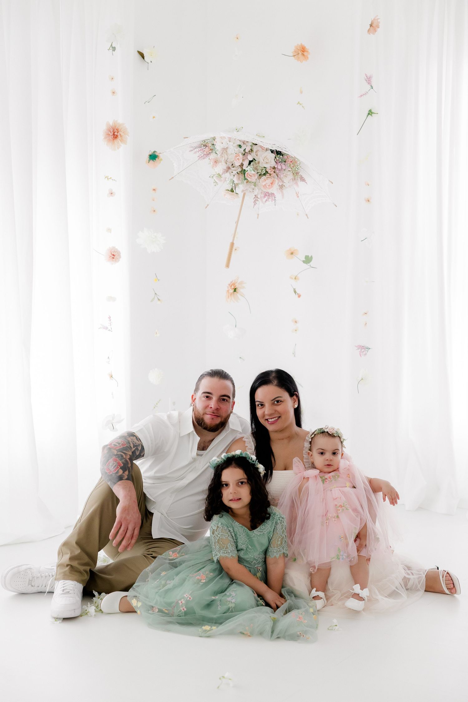 A family sits together on a white floor with delicate floral decorations falling from above.
