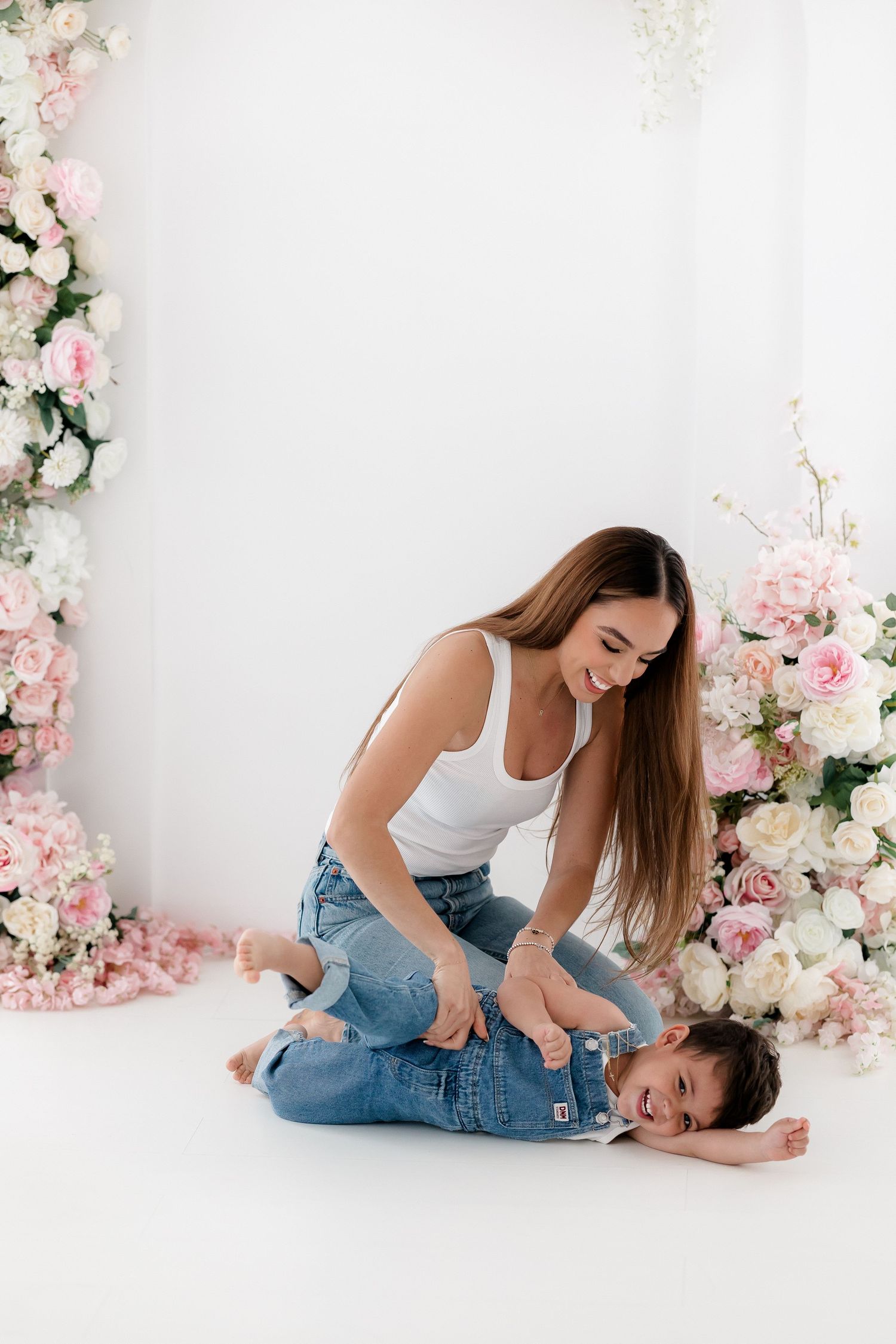 A parent and child share playful moments on a white floor surrounded by pink floral decorations.