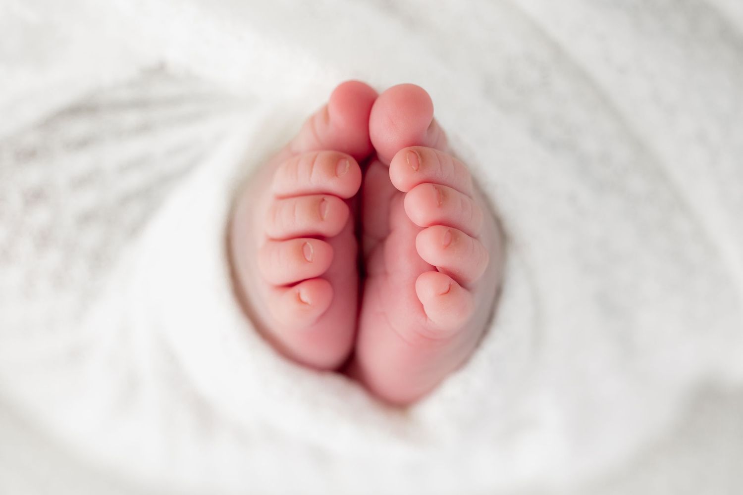Five close-up photos of tiny newborn baby feet arranged in a row on white fabric.