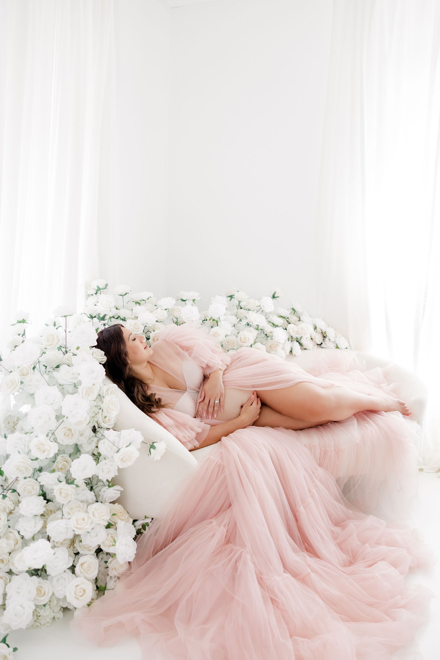 Ethereal pink tulle gown surrounded by white flowers in a dreamy boudoir setting.
