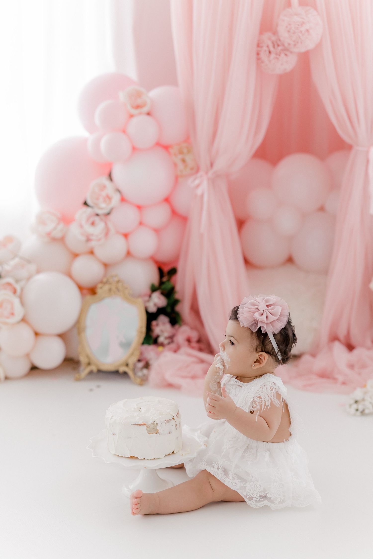Baby milestone photo with pink balloon arch and tulle decorations.