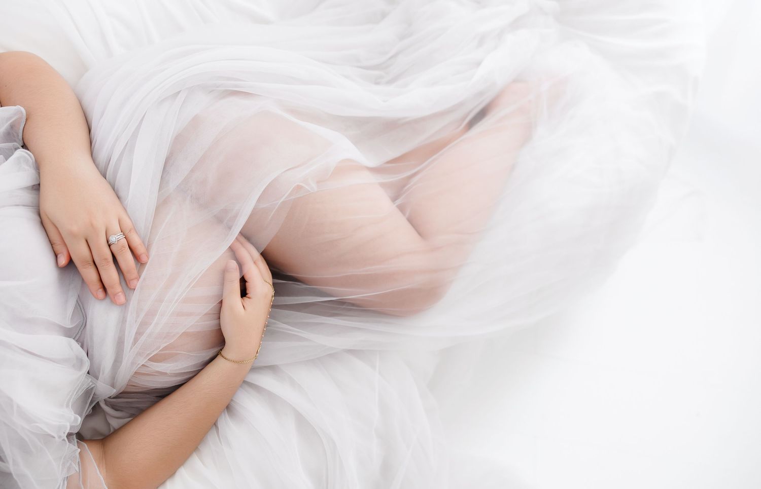 A person in white lace dress lying gracefully on a light background with flowing fabric around them.