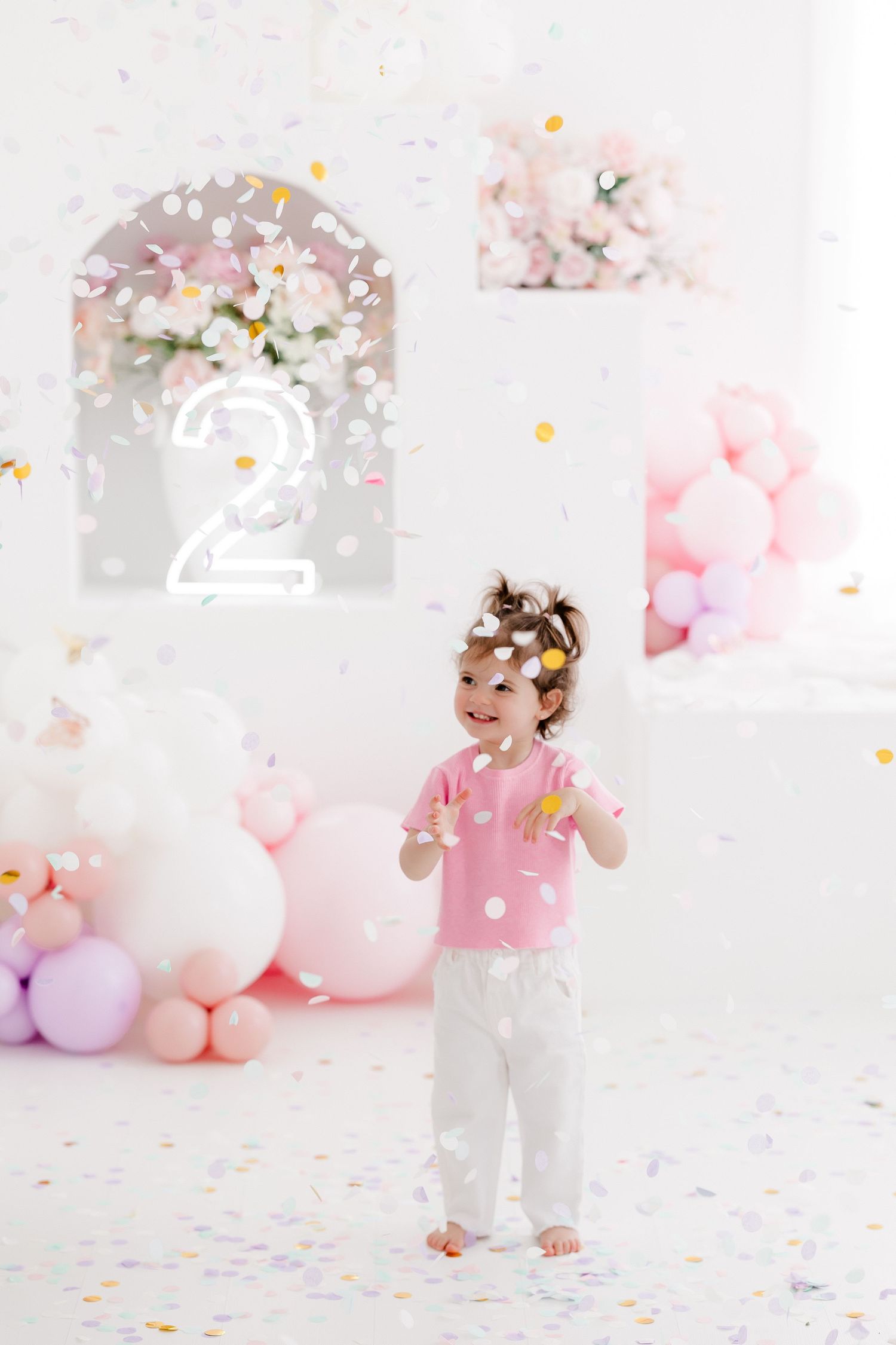 A festive party scene with pink and white balloons, confetti, and soft pastel decorations creating a dreamy celebration atmosphere.