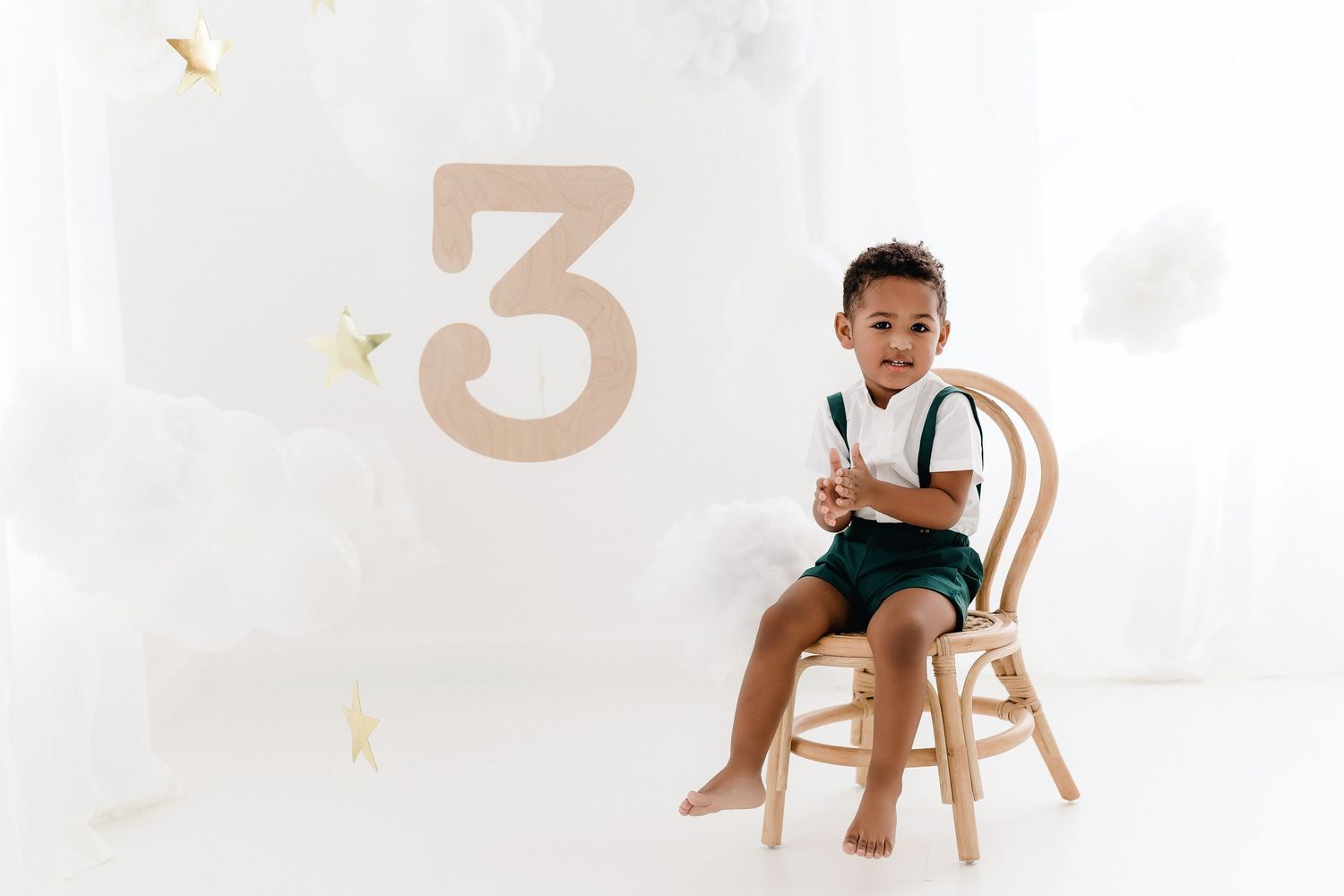 A young boy sits on a white chair against a minimalist white background in a professional studio setting.