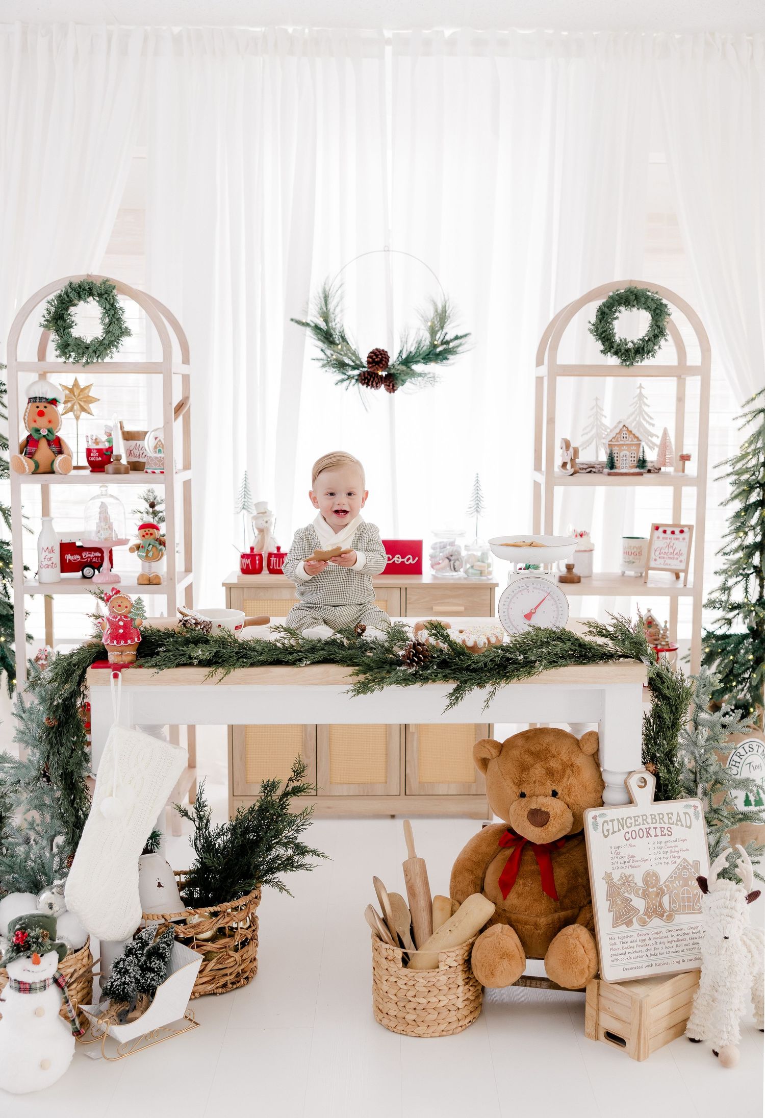 White Christmas themed setup with shelves, wreaths, garlands, and a teddy bear creating a cozy holiday display.