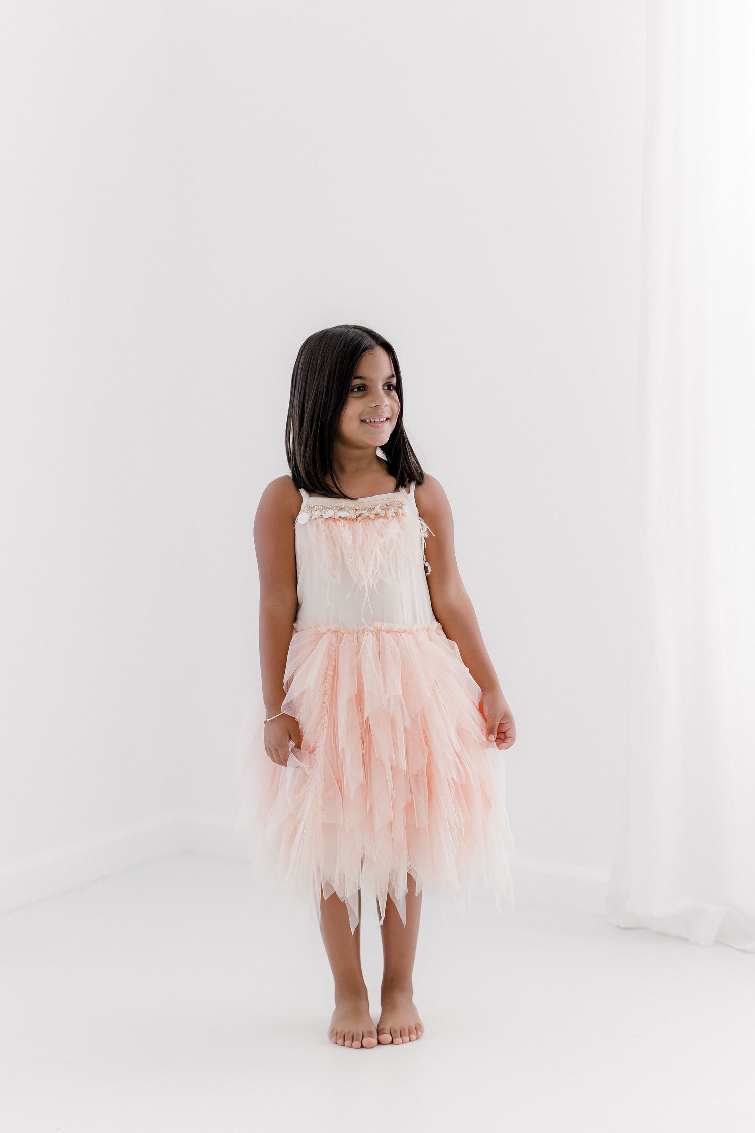 Dancer in white and peach tulle dress poses gracefully against white backdrop.