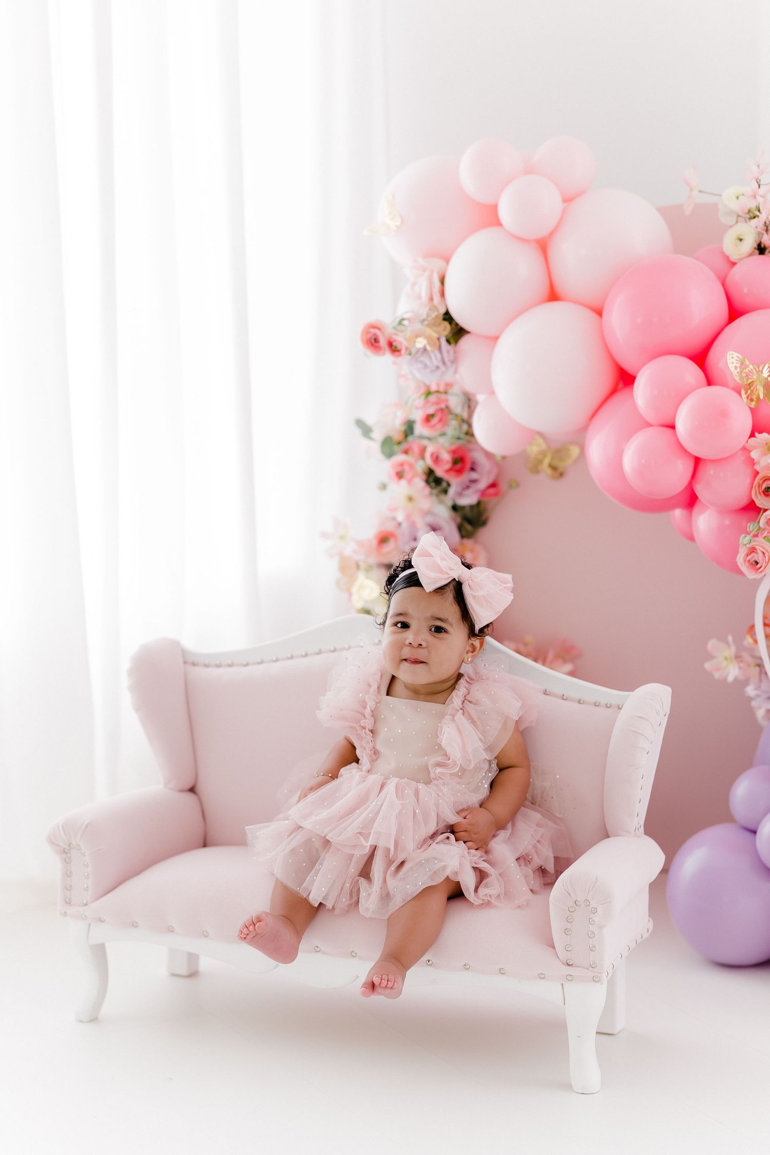 Elegant pink and white studio setup with vintage chaise lounge and balloon arch.