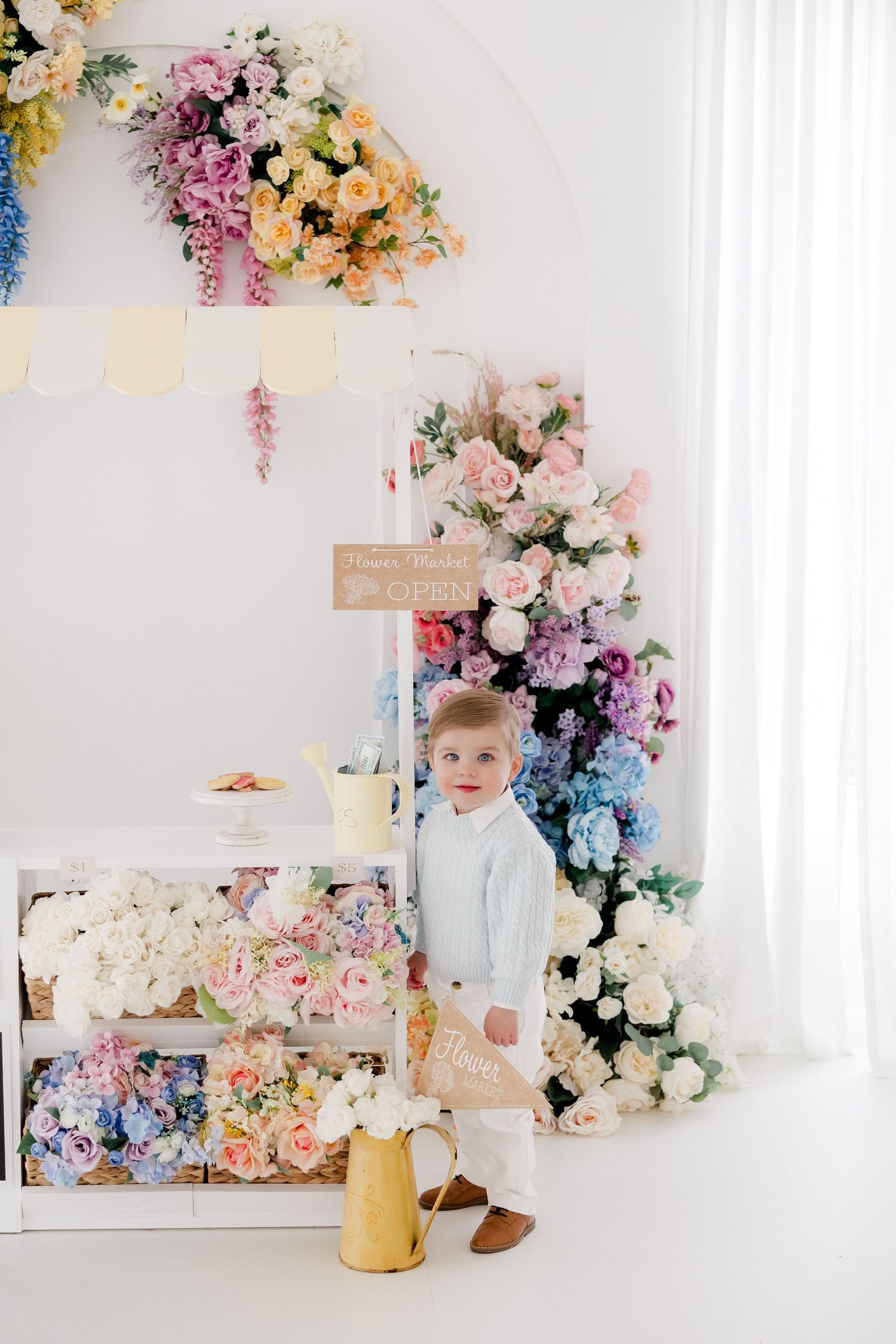 Elegant floral arch with pastel roses and blooms decorates a bright white room with vintage decor and artwork.
