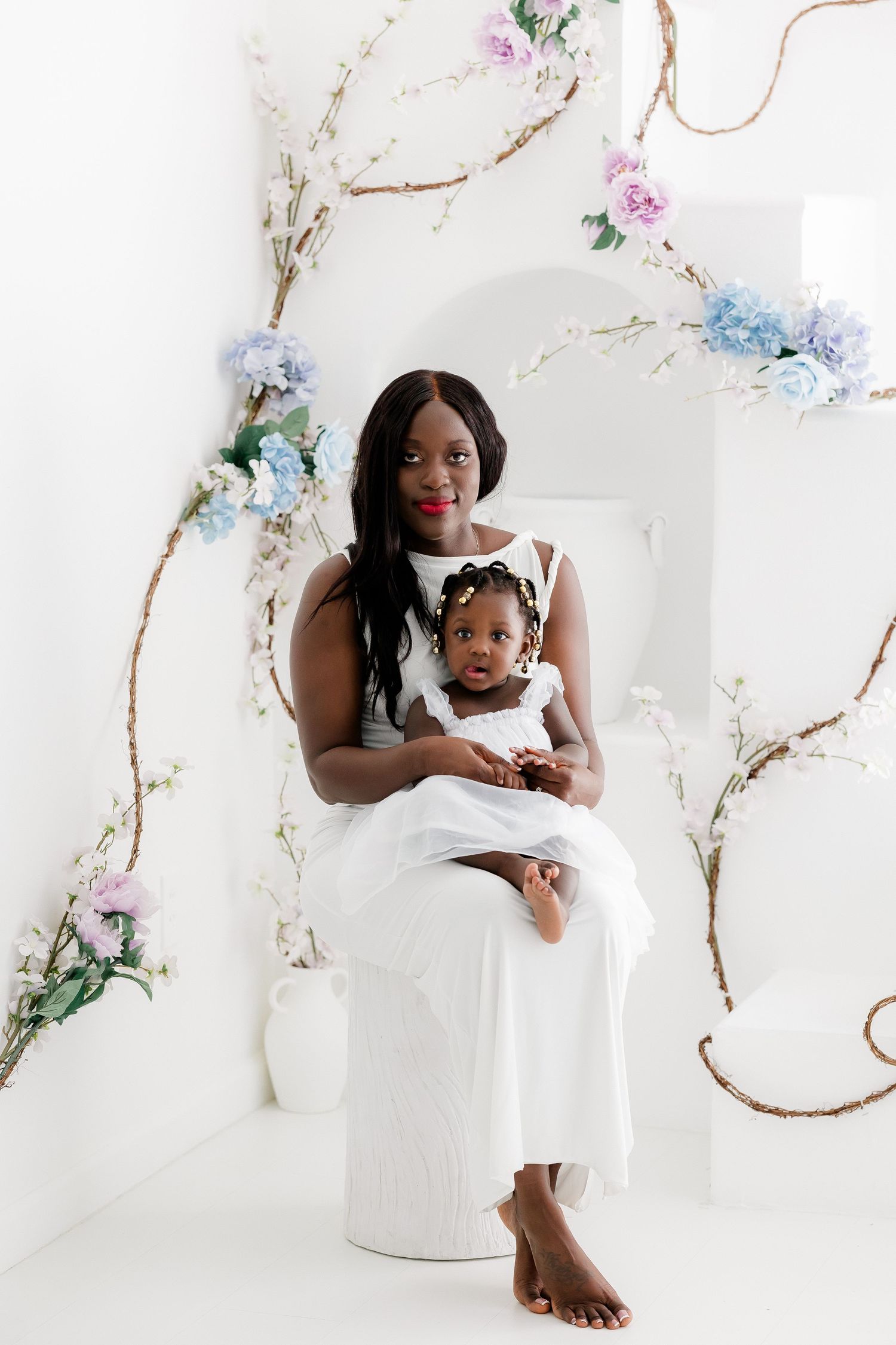 A white studio photo session featuring delicate floral decorations and natural elements creating an ethereal atmosphere.