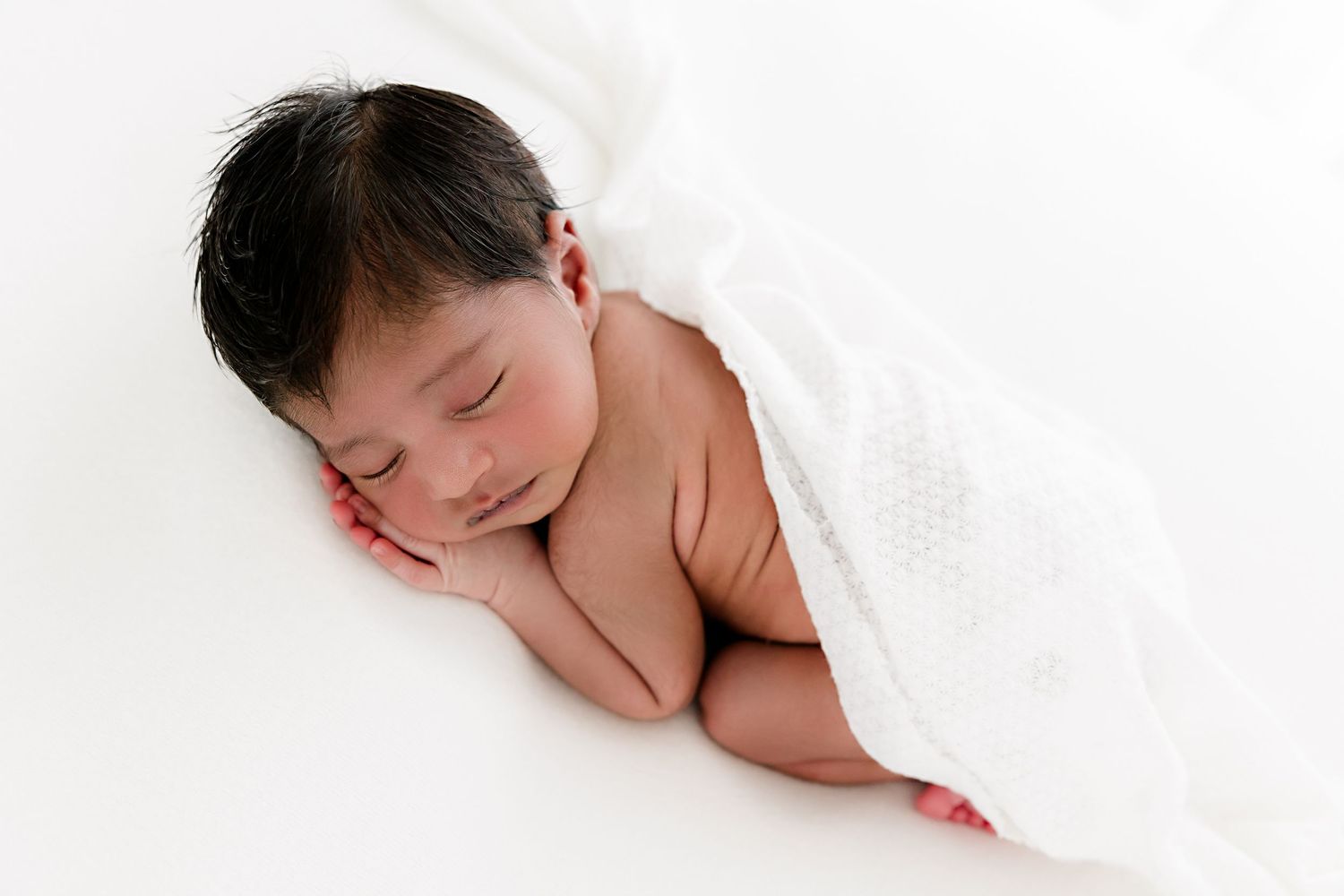 A sleeping newborn baby wrapped in soft white fabric lies peacefully on a white background at a New Jersey photo studio