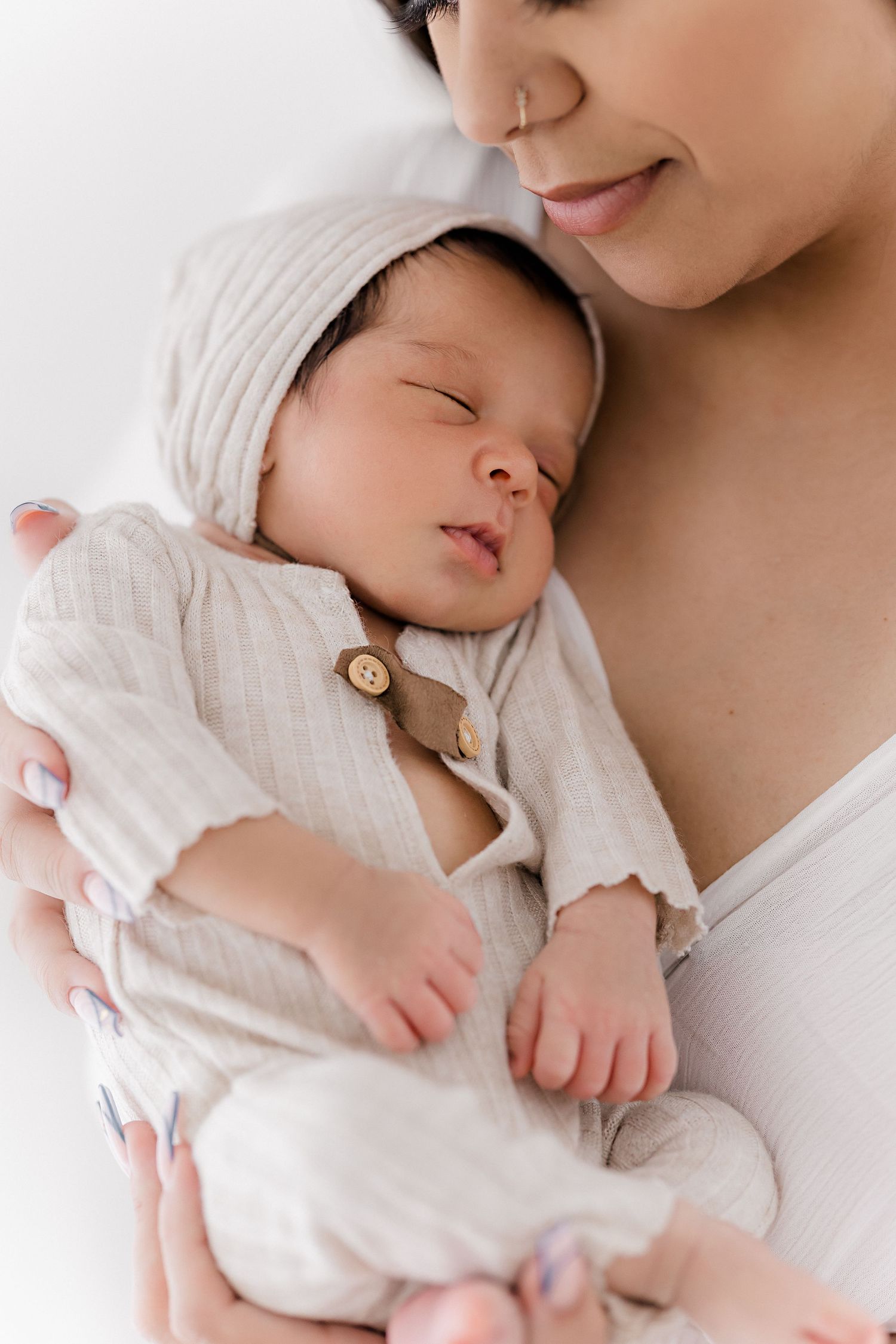 A newborn baby in white clothing sleeps peacefully while being cradled in gentle arms.