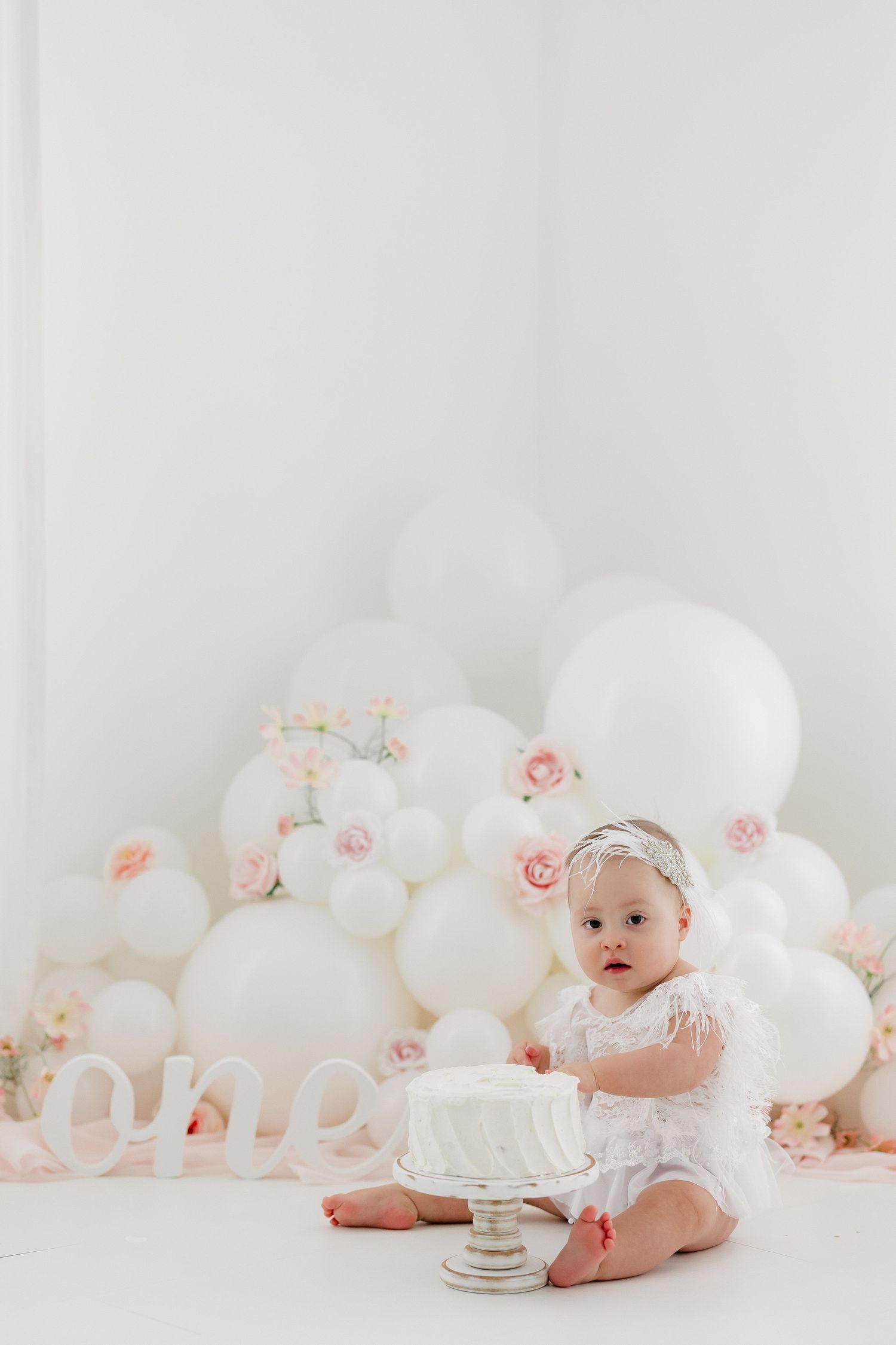 White balloon arch and floral decorations create an elegant backdrop for a baby's milestone photo session.