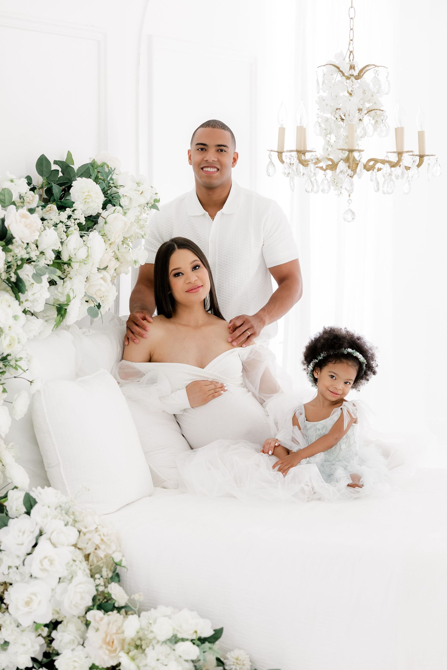 Family maternity portrait in all-white studio with floral decorations.