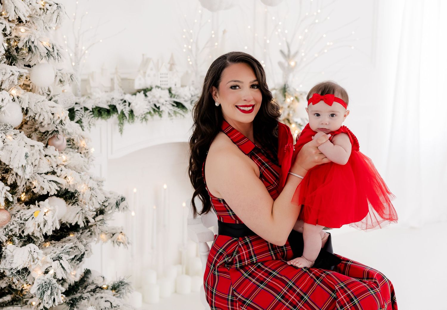 Christmas portrait session with red and white outfits against decorated white trees.