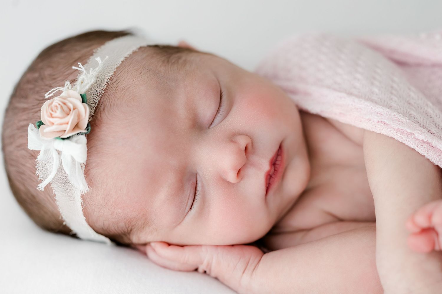 A sleeping baby wearing pink lace clothing lies peacefully on white bedding.