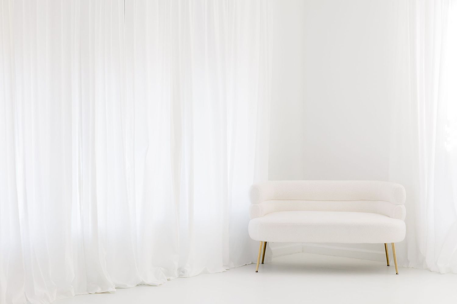 Minimalist white room interior with cream-colored mid-century modern bench against sheer curtained wall.